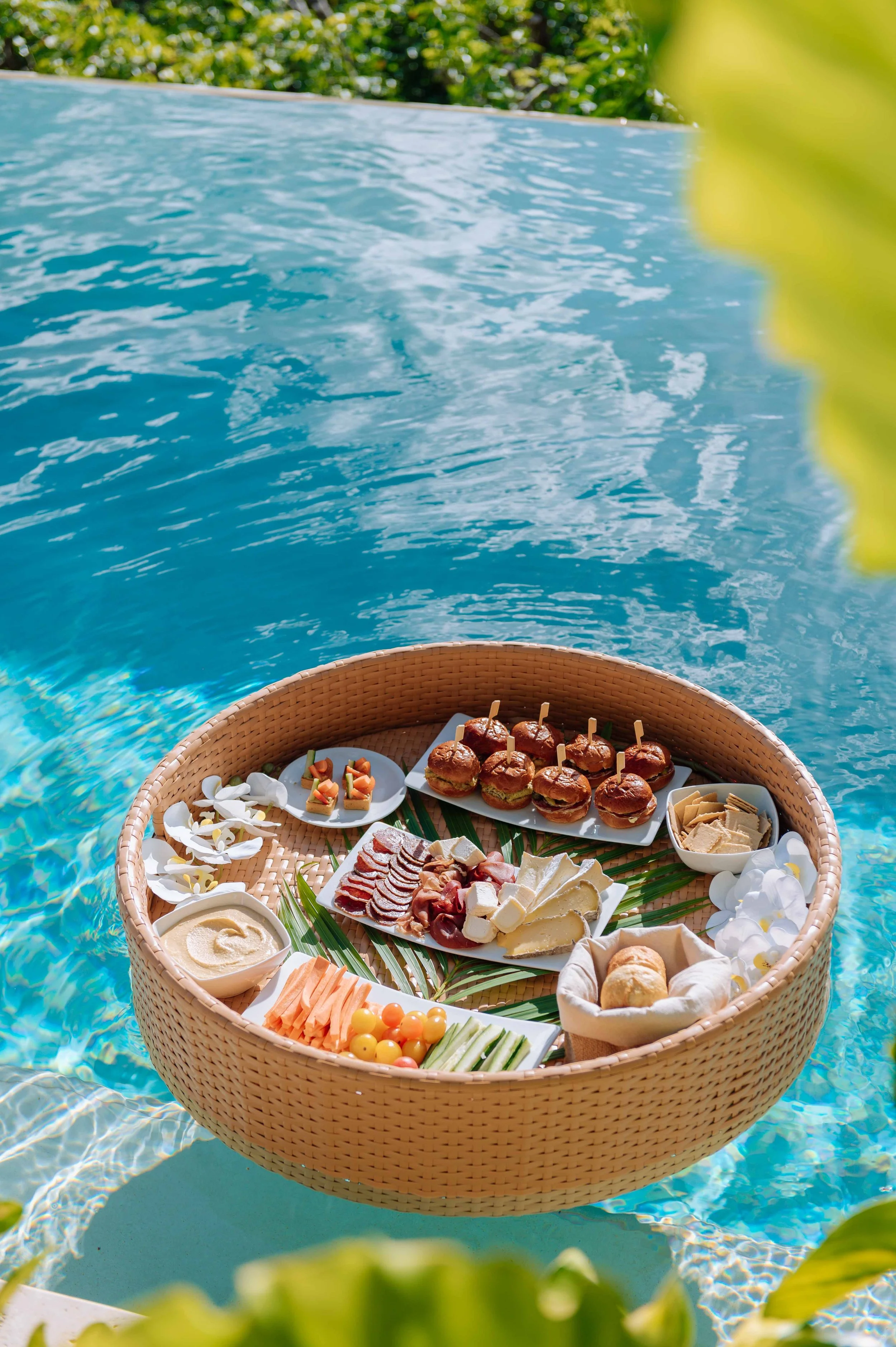 Plateau de nourriture en bord de piscine avec des amuse-gueules, légumes, fromages, et mini hamburgers.