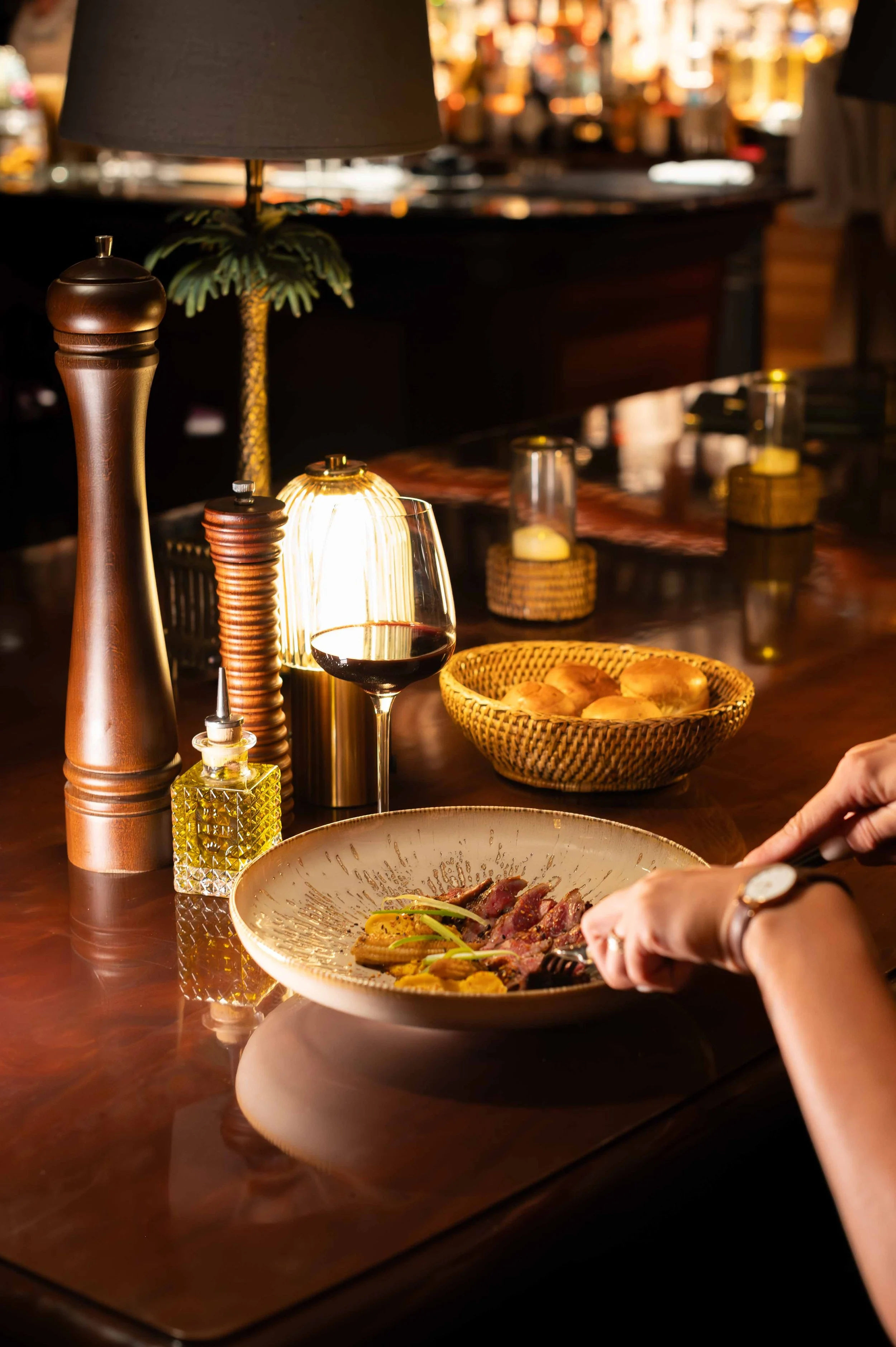 Un dîner dans un restaurant avec une assiette de viande, un verre de vin rouge, et un décor chaleureux avec des lampes, un panier de pain et des accessoires en bois.