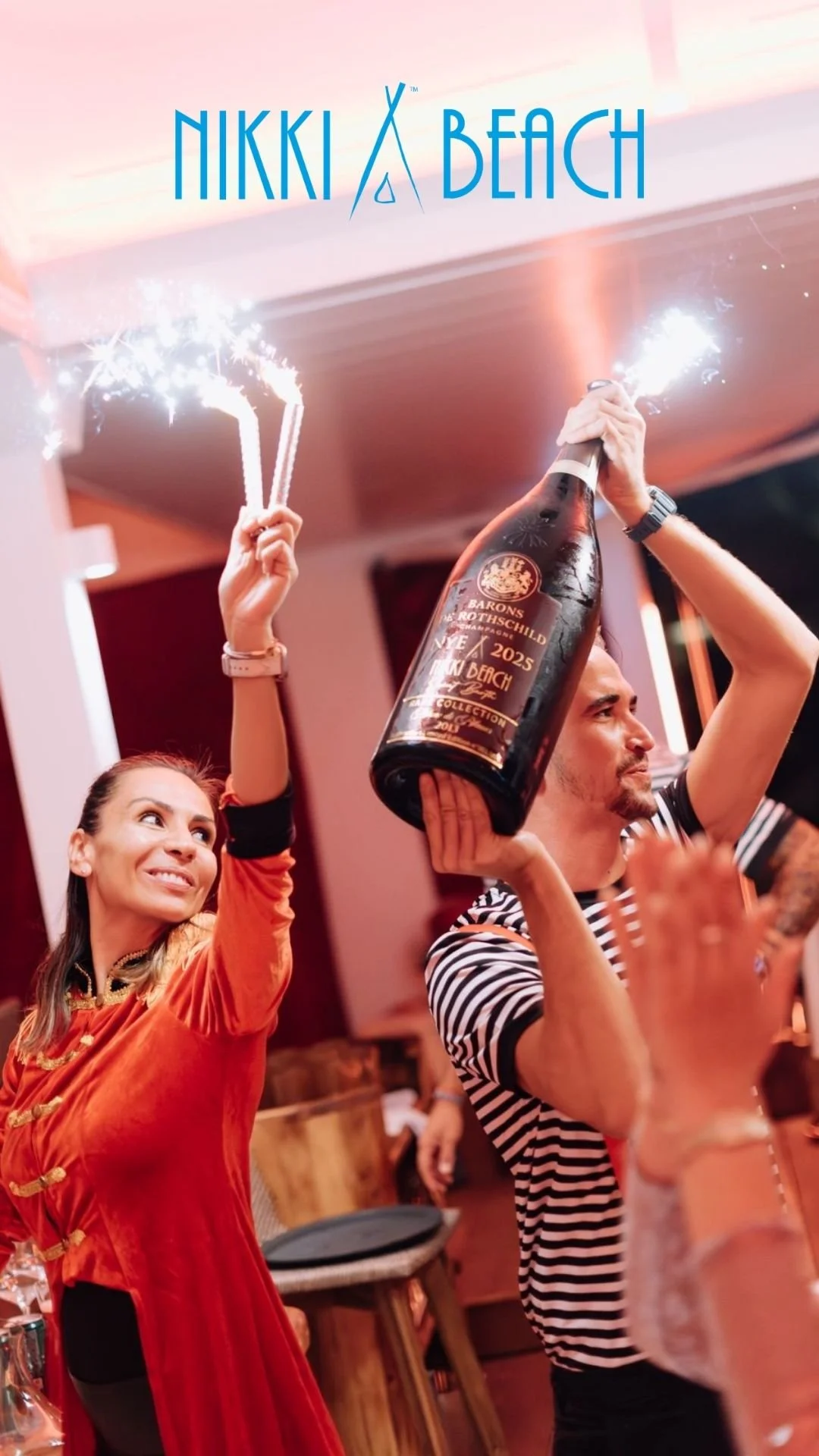 Deux personnes célébrant avec des bouteilles de champagne et des sparkler lors d'une fête au Nikki Beach.