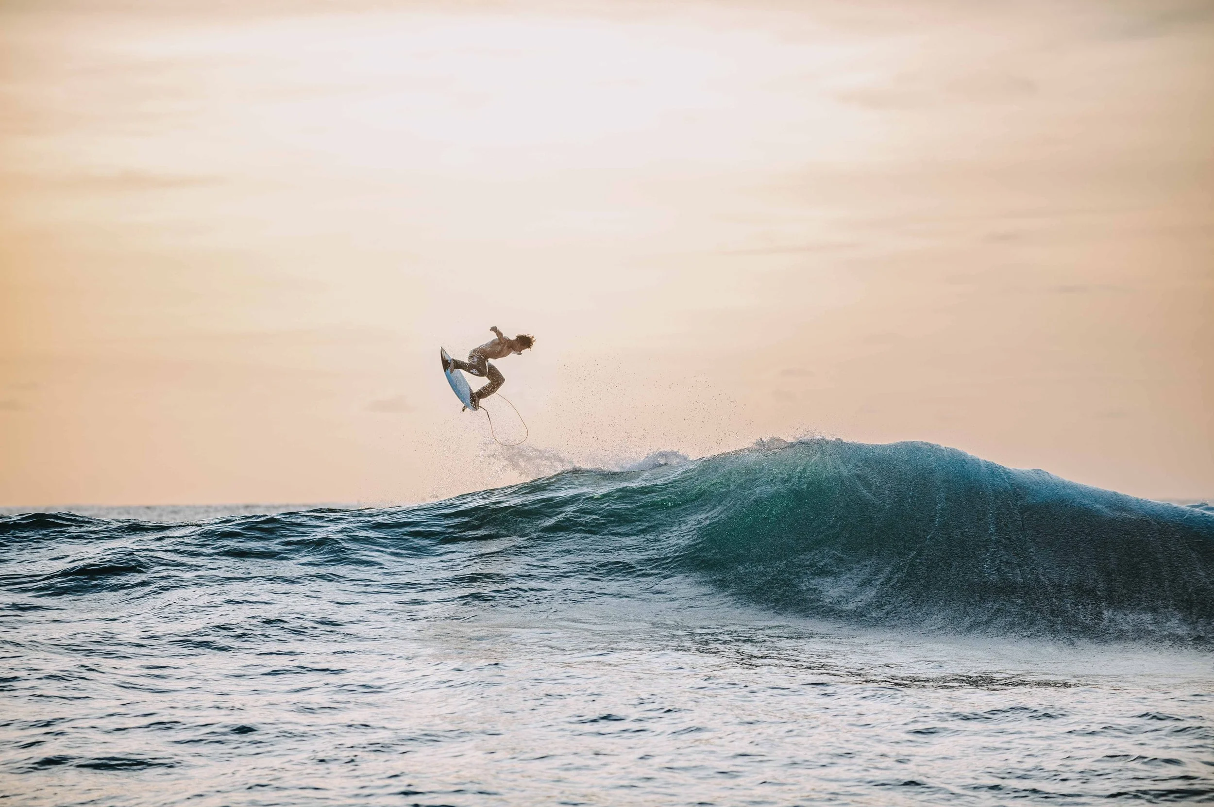 Un surfeur en train de sauter au-dessus d'une vague en mer au coucher du soleil.