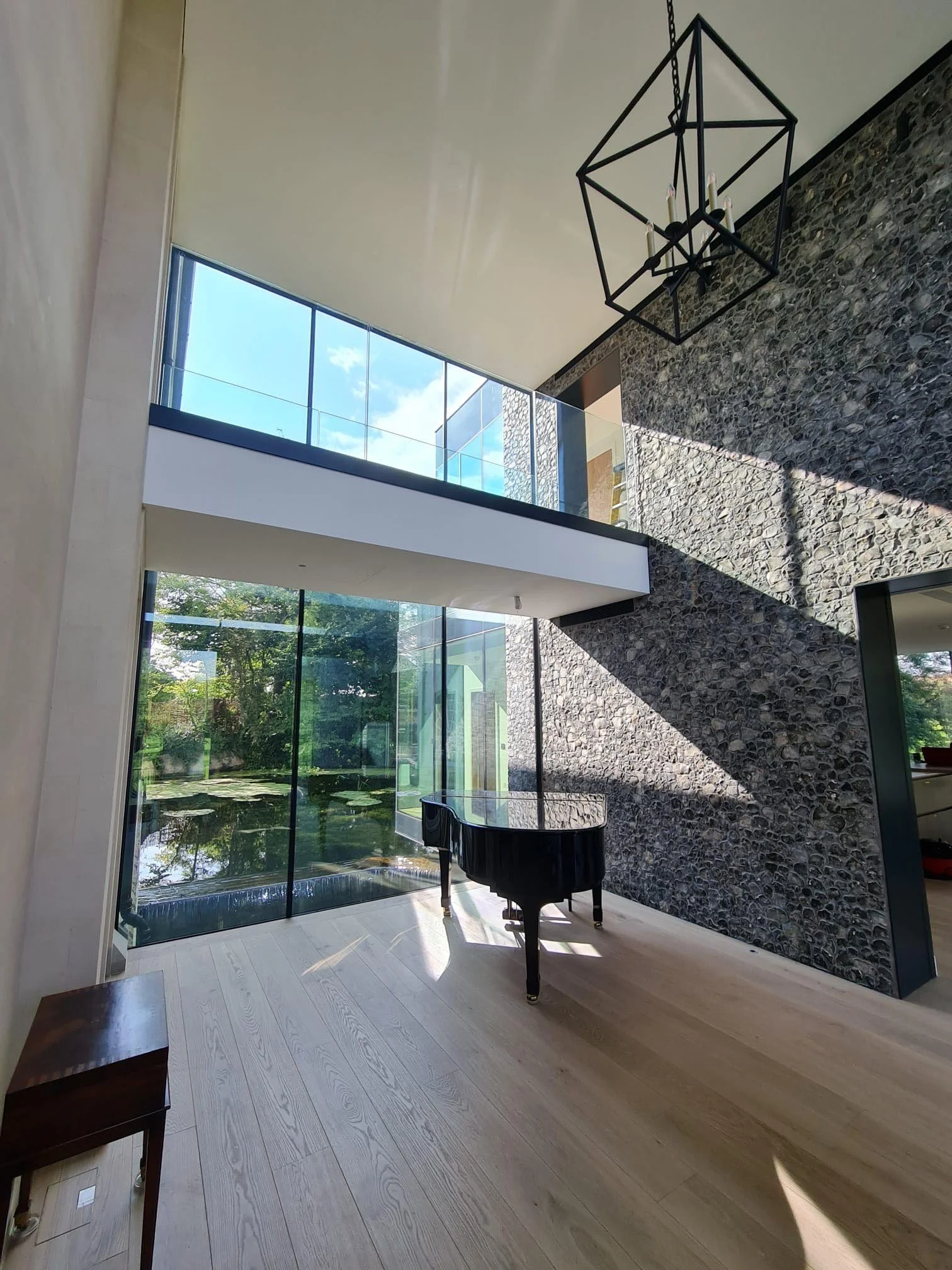 double height hallway with glazed walkway, large flint wall and black grand piano