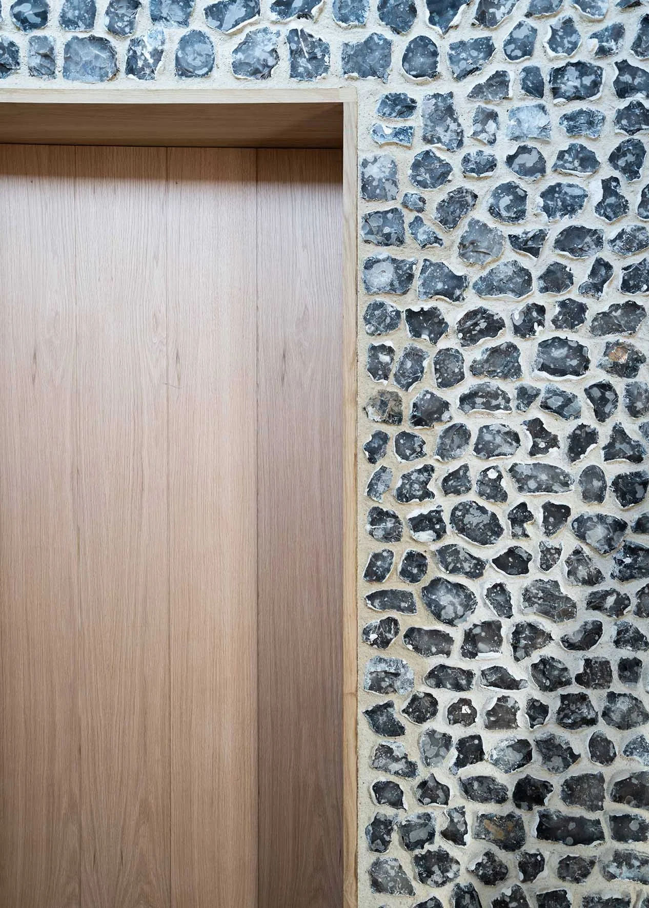 Close-up of a wooden elevator door next to a stone wall with dark and light gray stones set in white mortar.