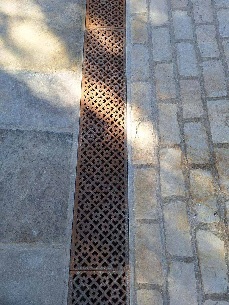 Close-up of a metal drainage grate between stone and brick pavement.