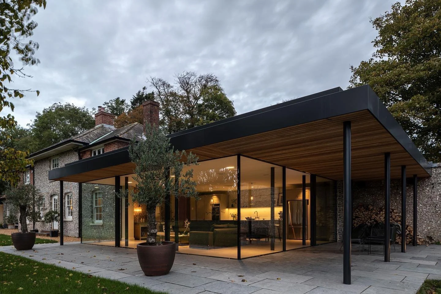 Modern house with a glass-walled outdoor patio, potted trees, and a backyard with grass and trees.