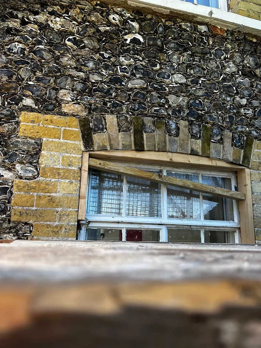 Close-up of a window set in a stone and brick wall, with the top of the wall showing black stones and bricks around the window frame.
