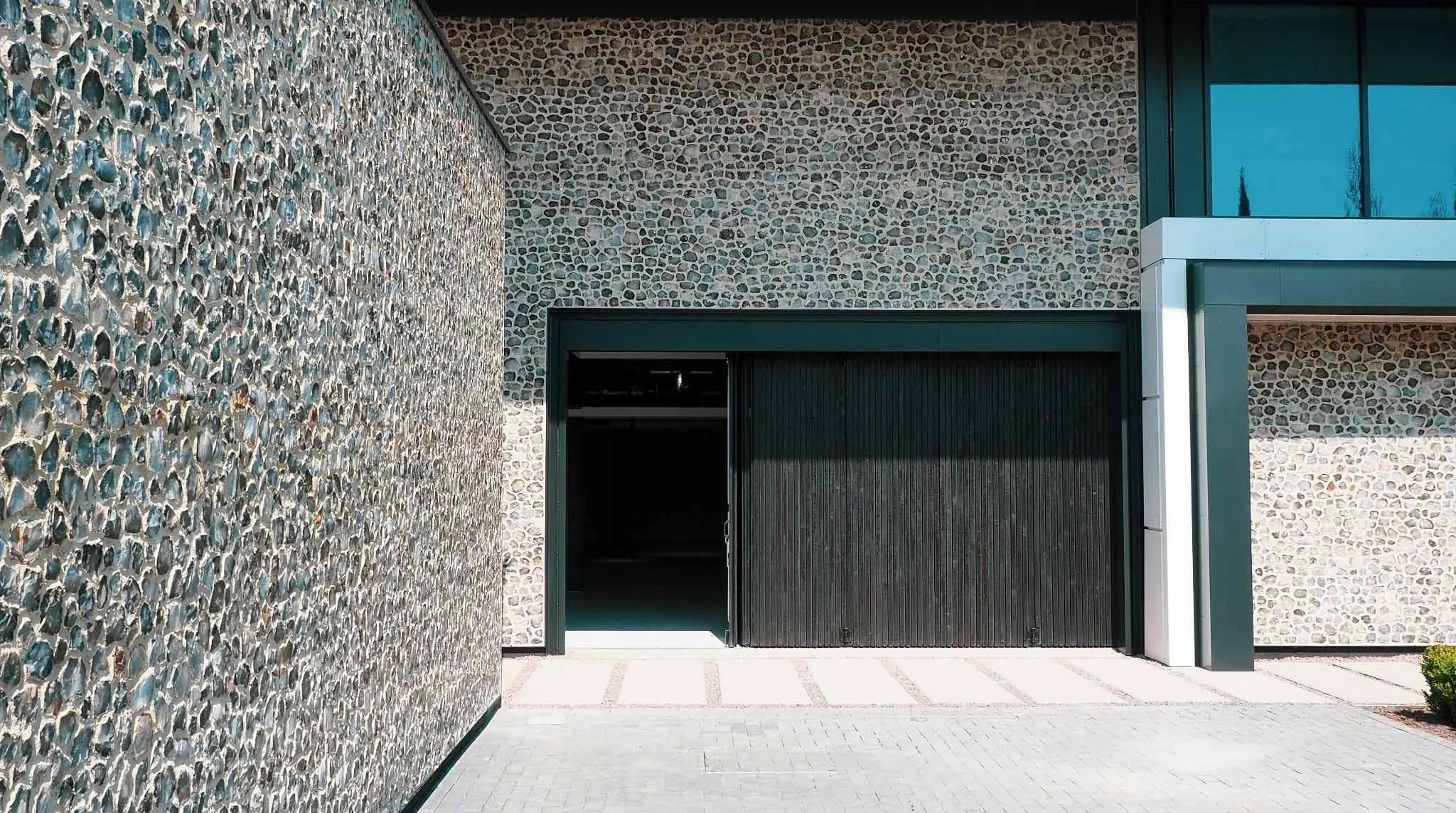 Modern building exterior with a textured stone wall, a garage door partially open, and a large window above.