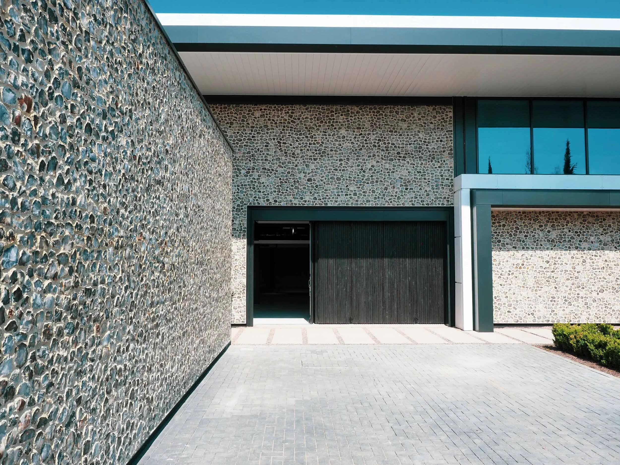 Modern building exterior with a pebble stone wall, large glass windows, and a paved walkway.
