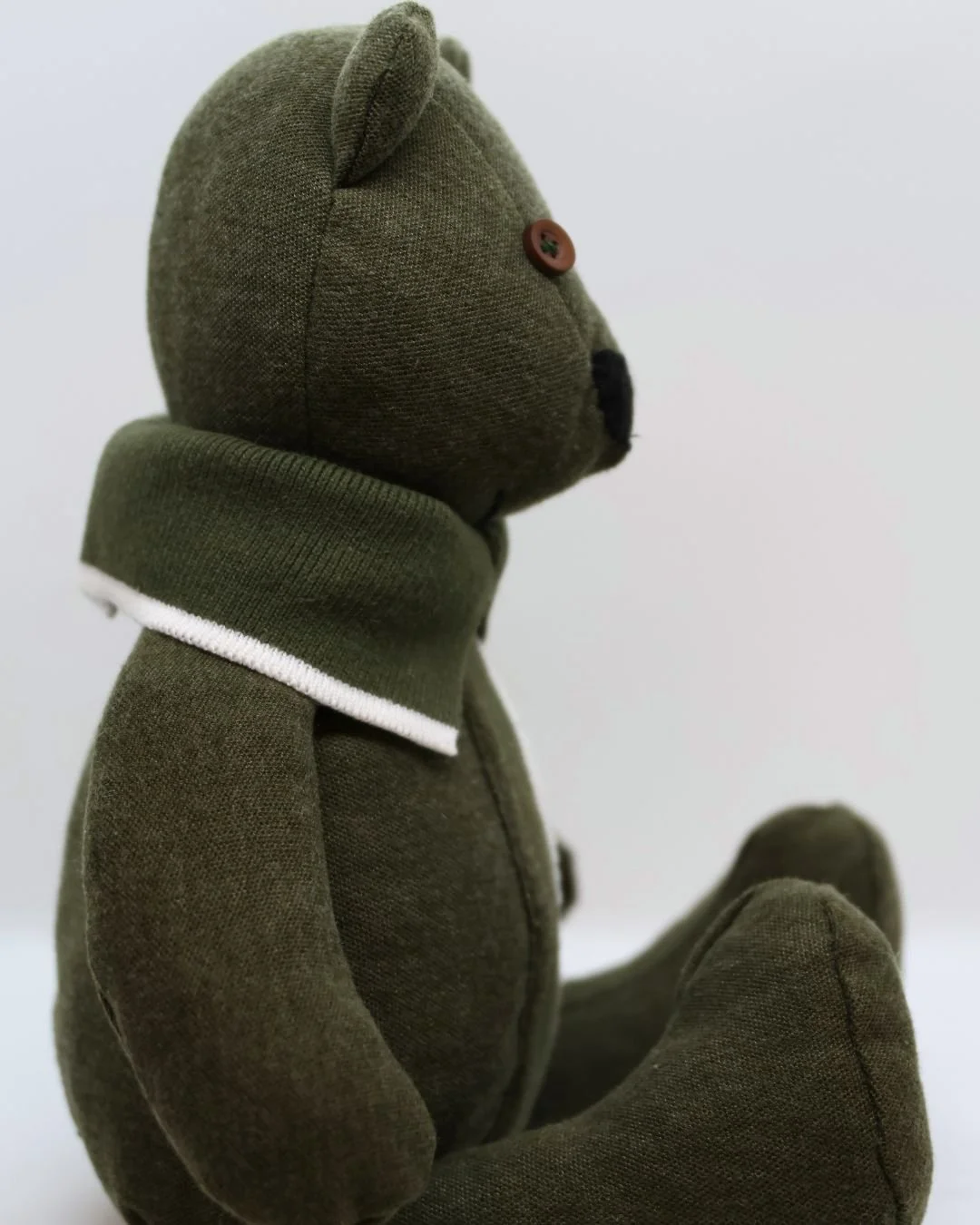 Peluches de oso en color verde con detalles en blanco y negro, sentado, de perfil.