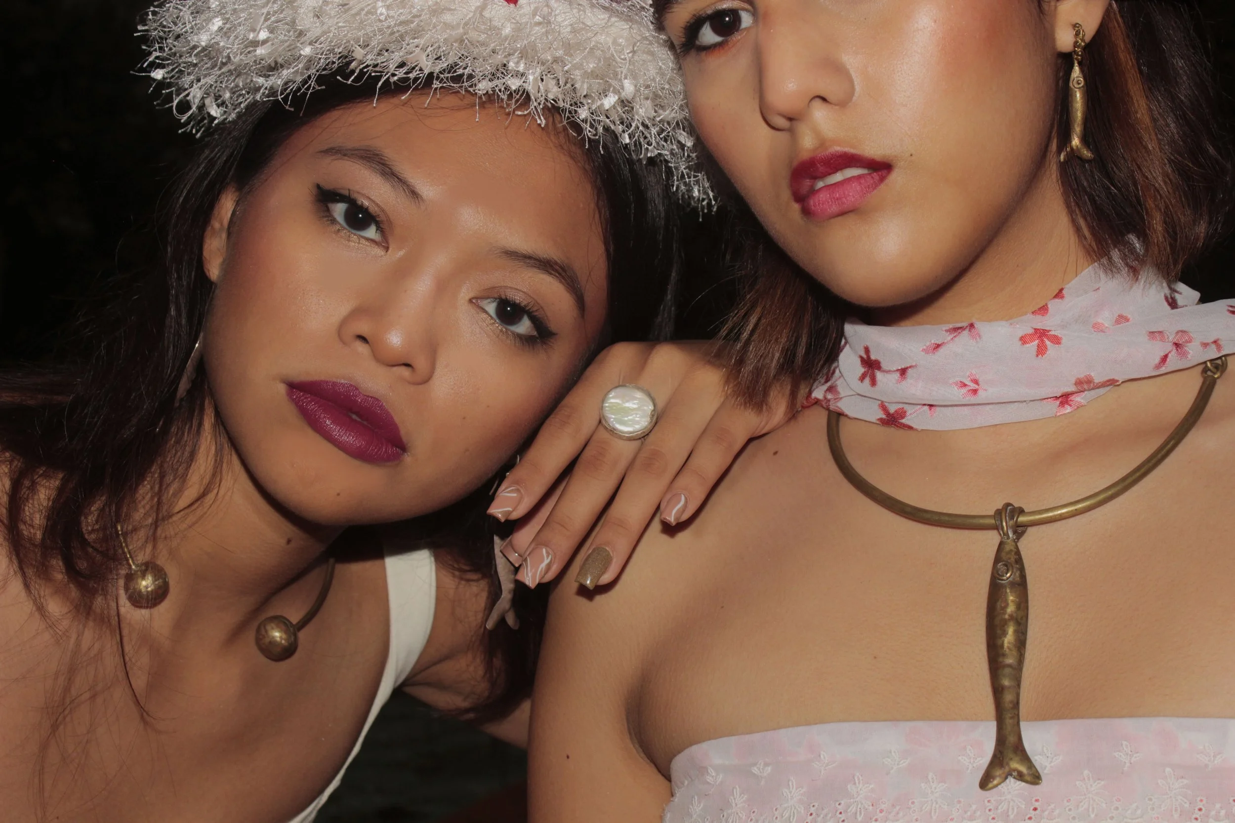 Dos mujeres con accesorios de joyería y ropa de verano, una de ellas con sombrero de fiesta y la otra con bufanda de seda con estampado floral.
