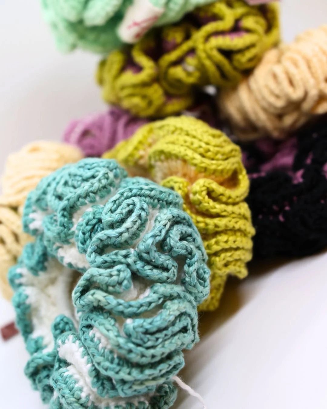 Lote de scrunchies de colores en diferentes tonos y texturas, hechos con tela y ganchillo.