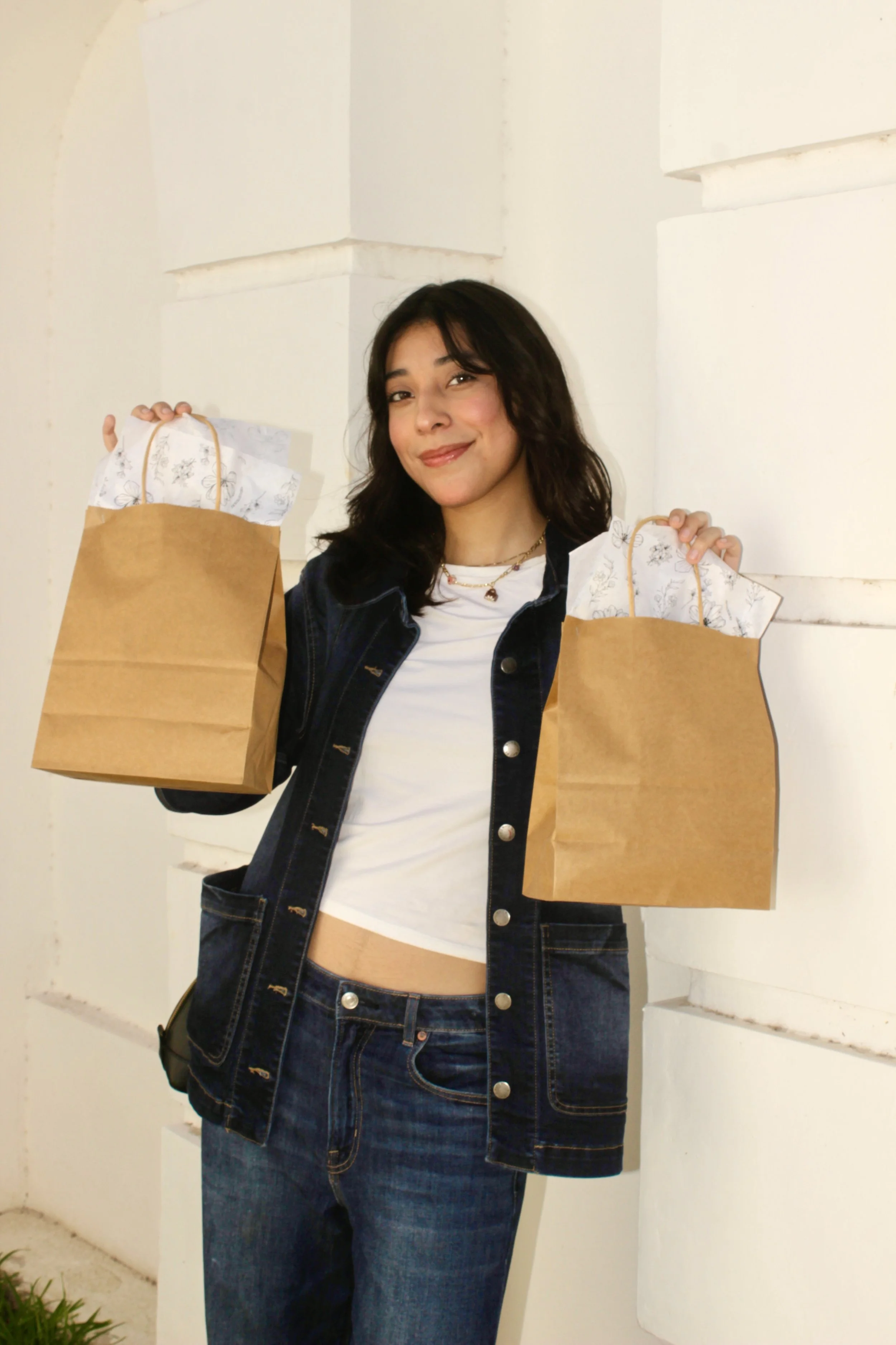 Joven sonriendo, sosteniendo bolsas de papel con papel decorativo en el interior, usada para compras.