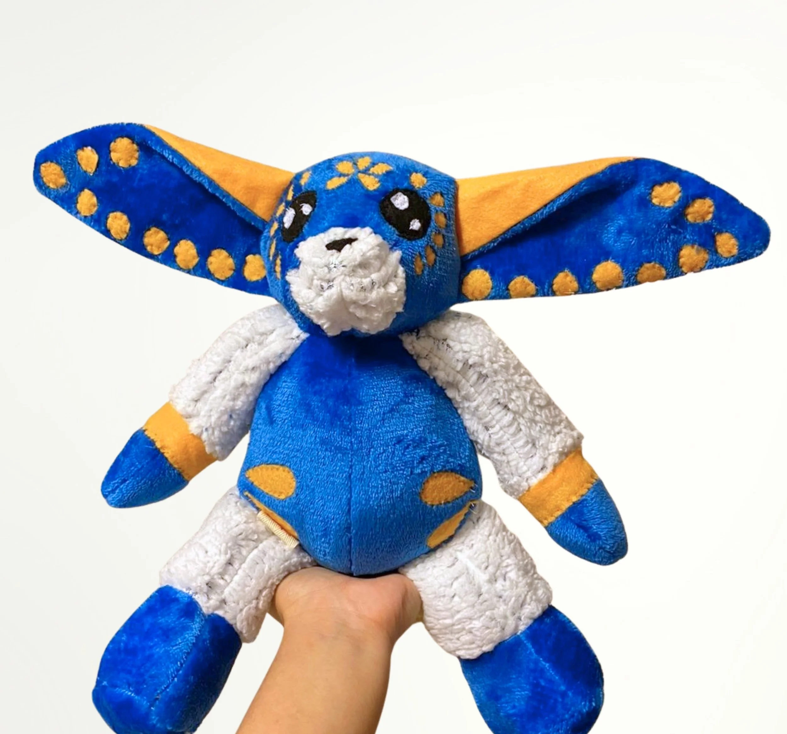 Pelucha de un murciélago con colores azul, blanco, naranja y negro.