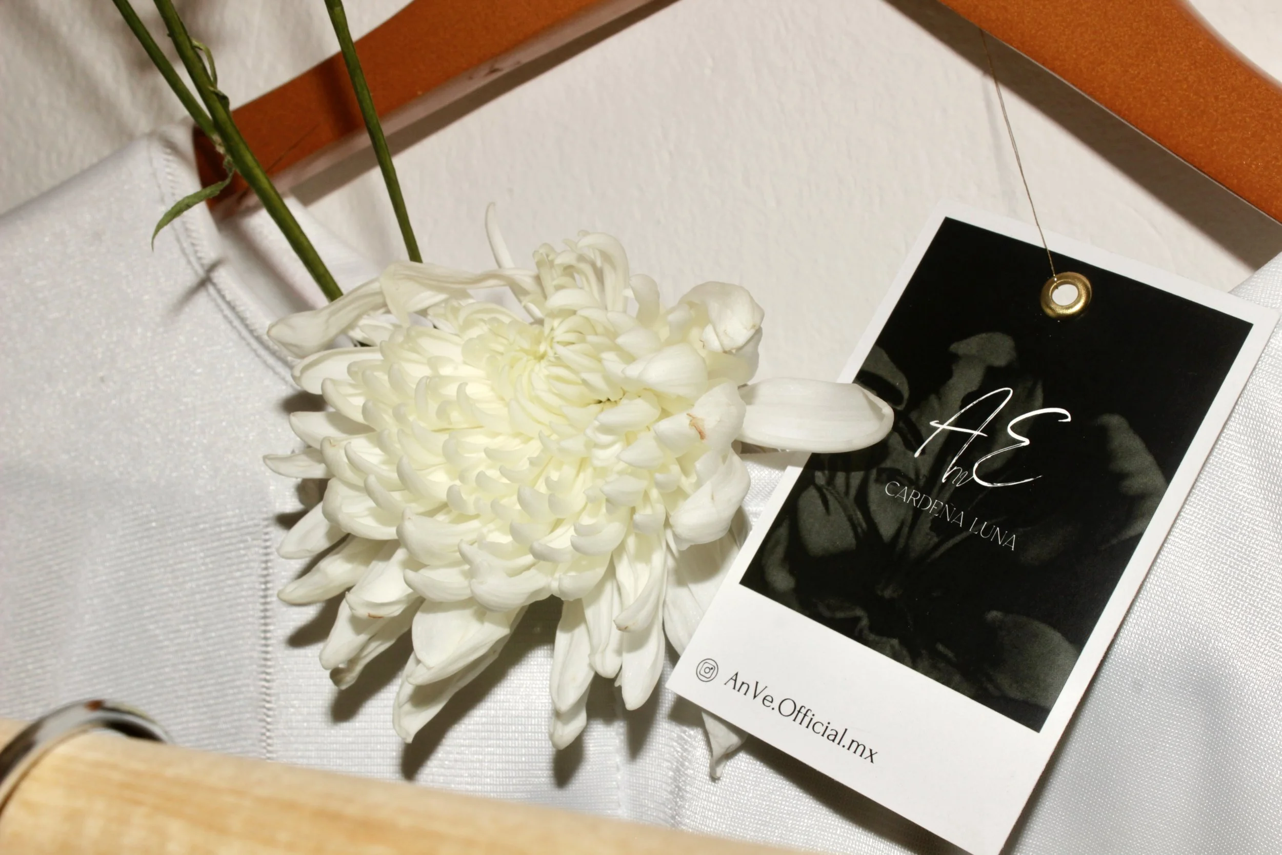 Flores blancas y una camisa en un gancho de madera con una etiqueta de ropa