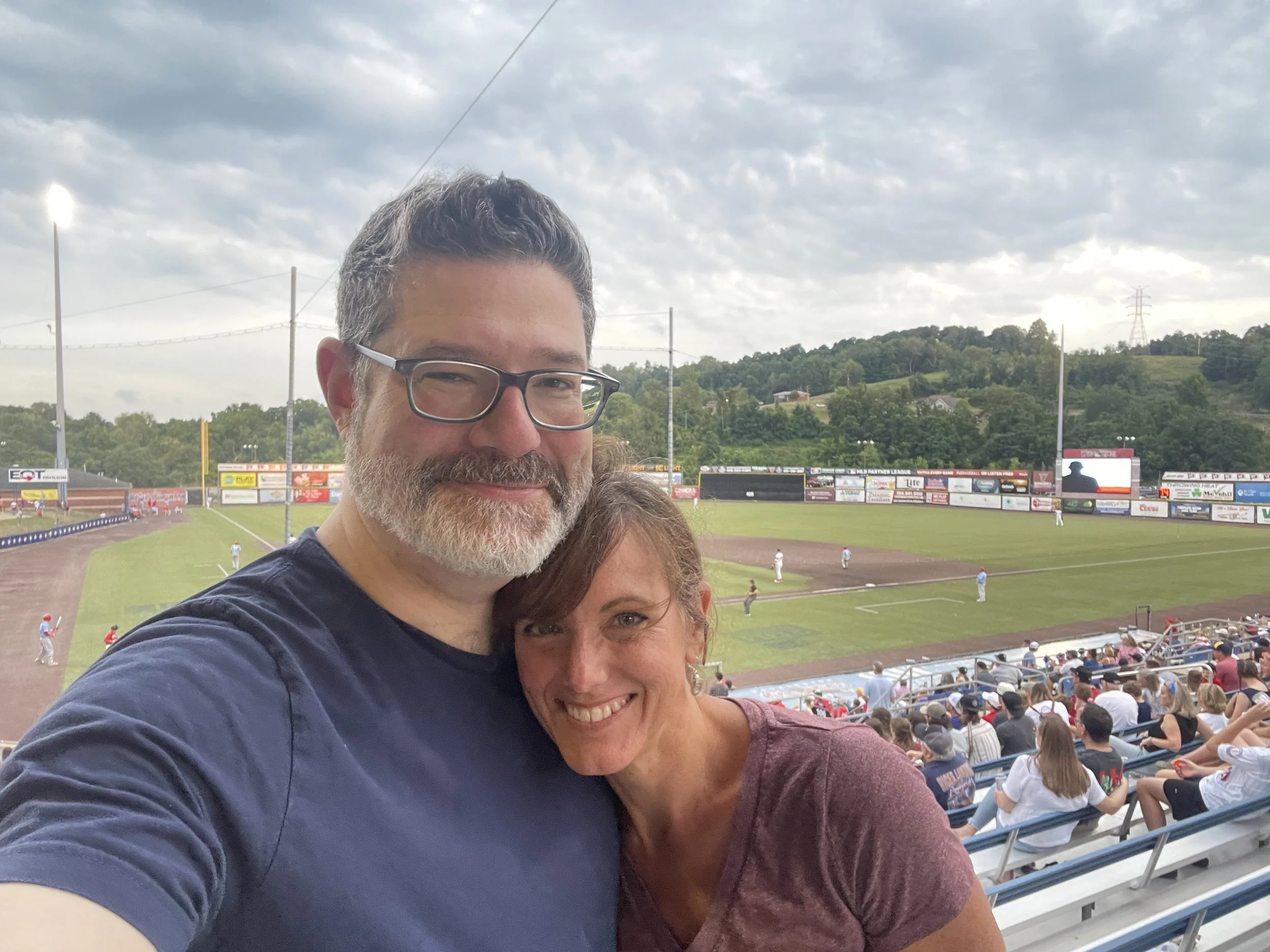 Rebecca and her husband Scot MacTaggart at a Washington Wild Things baseball game at EQT Park with the field and spectators in the background.