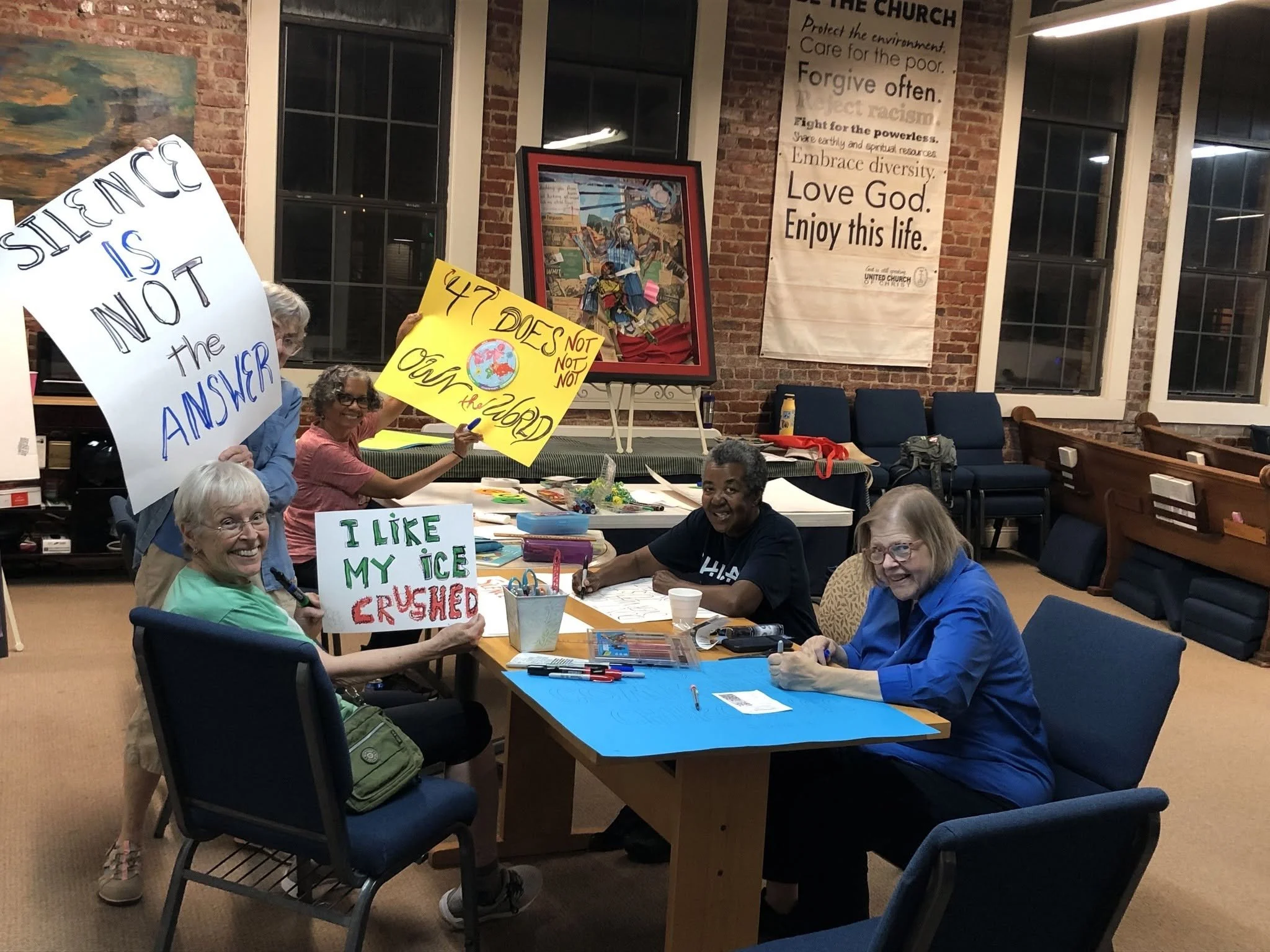 a group of people are at a table making signs, some are holding them in the air and they read silence is not the answer and I like my ice crushed
