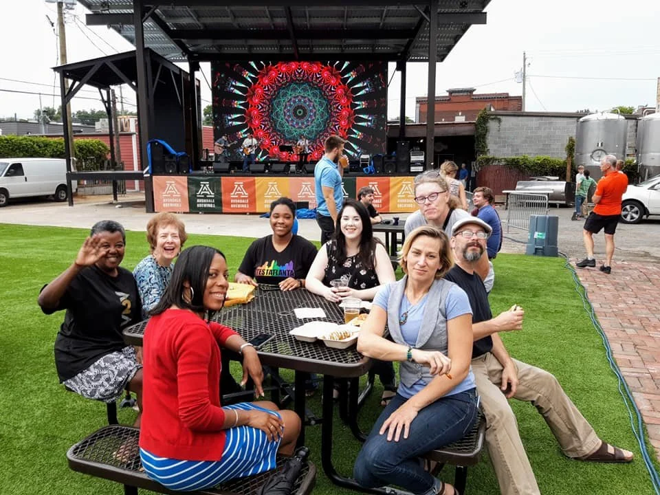a group of people are sitting at an outdoor table with a stage in the background