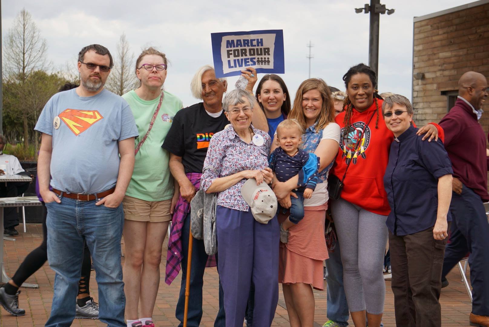 a group of people of various ethnicities and ages are standing together outside with a sign being held behind them that says march for our lives