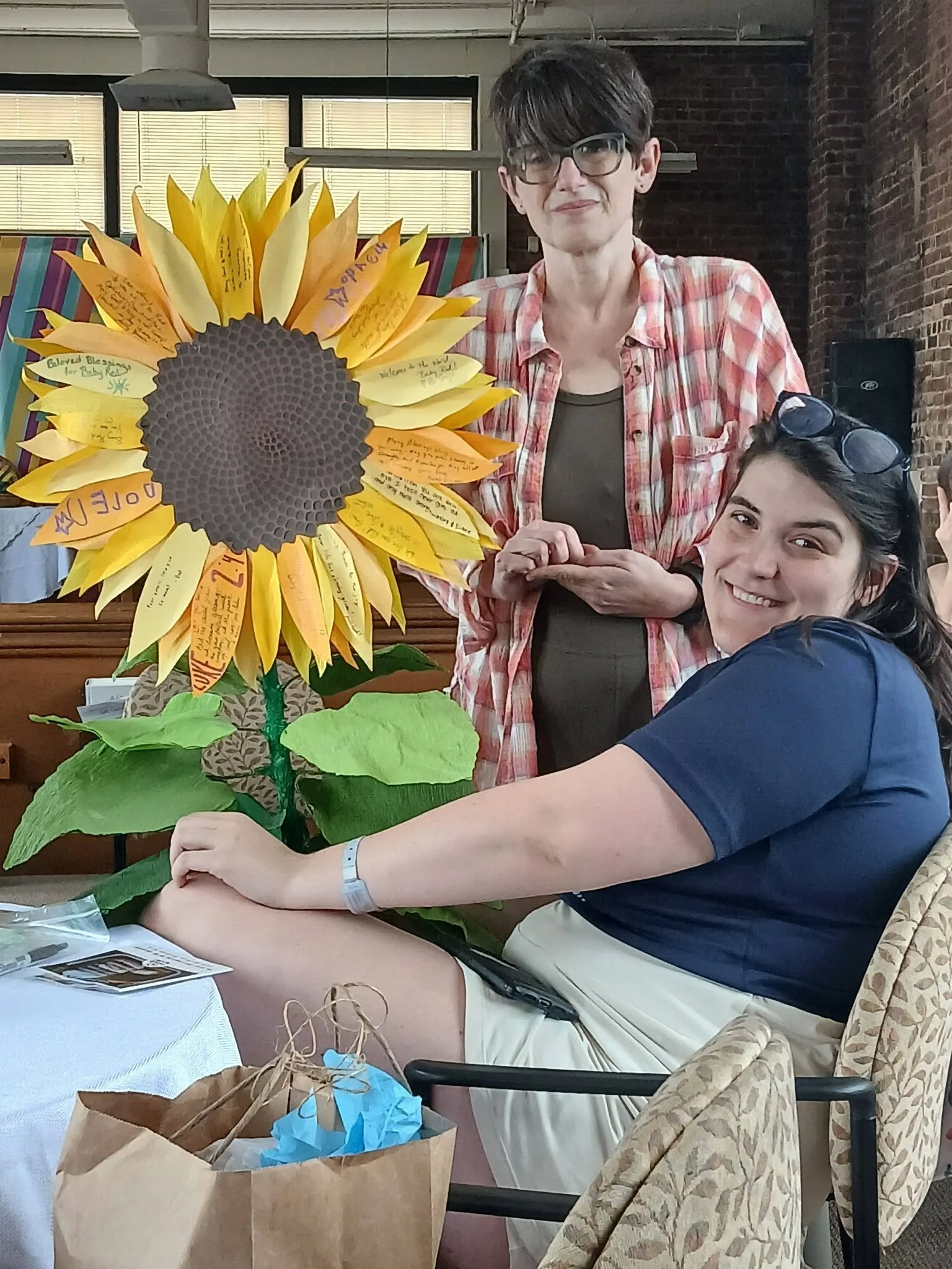 two people next to a large paper sunflower