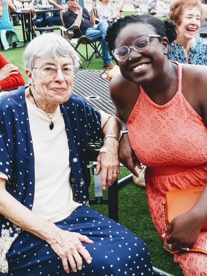 two people are sitting outside together smiling with a crowd in the background