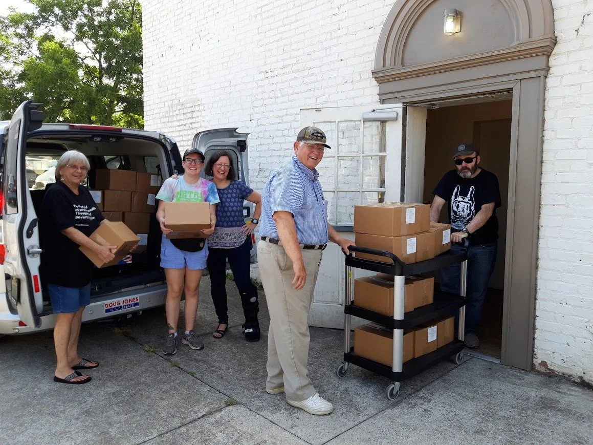 a group of people are standing outside a building loading brown boxes into a white van