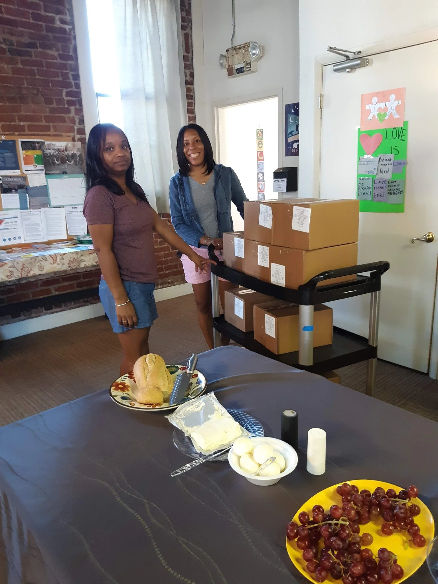 two women are standing next to a cart with several cardboard boxes on it