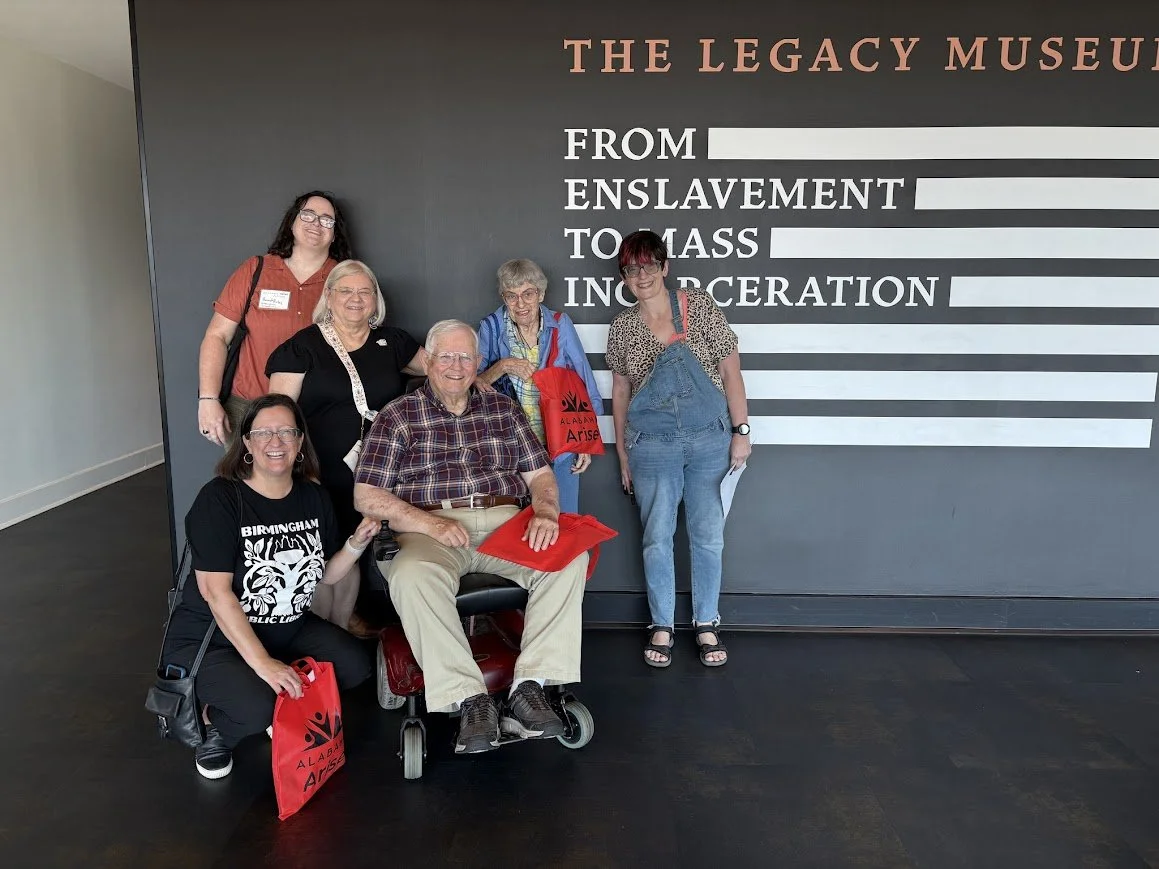 a group of people standing in front of a sign that says The Legacy Museum from Enslavement to Mass Incarceration