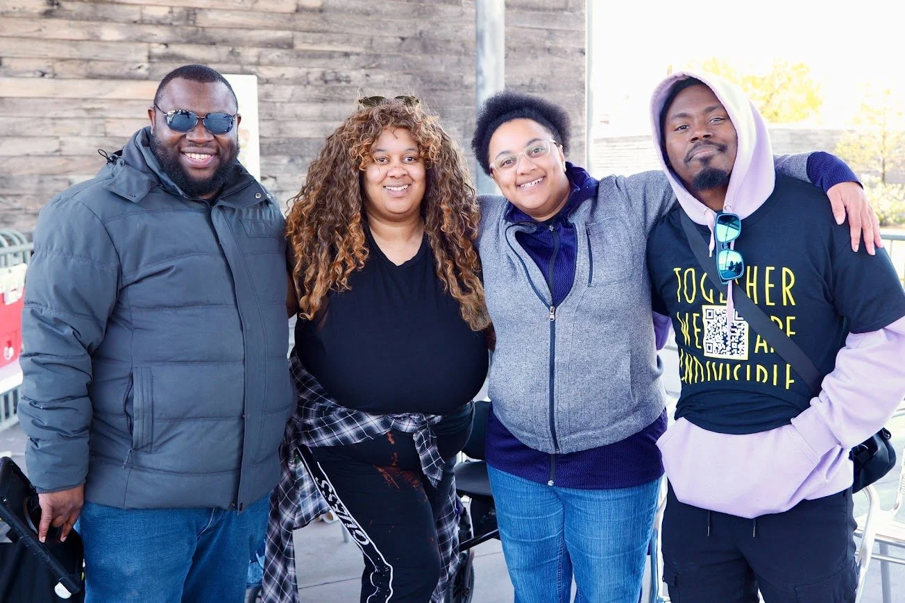 four people are standing and smiling with their arms around each other