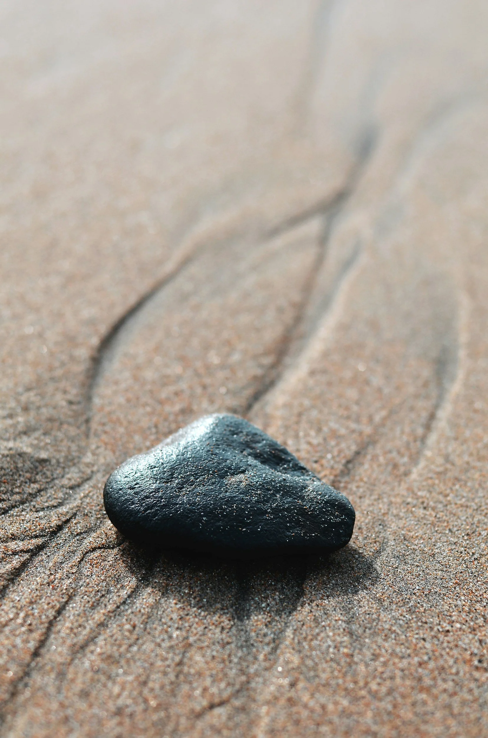 A black stone on sandy beach with faint engraved lines.