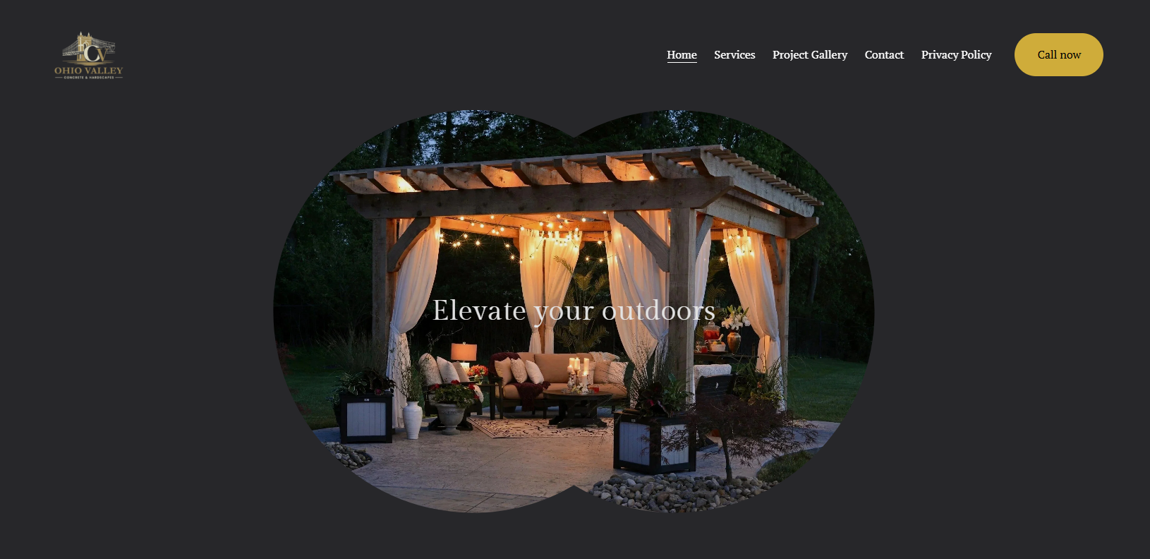An outdoor sitting area under a wooden pergola with string lights and drapes, featuring a sofa, tables, and potted plants, at dusk.