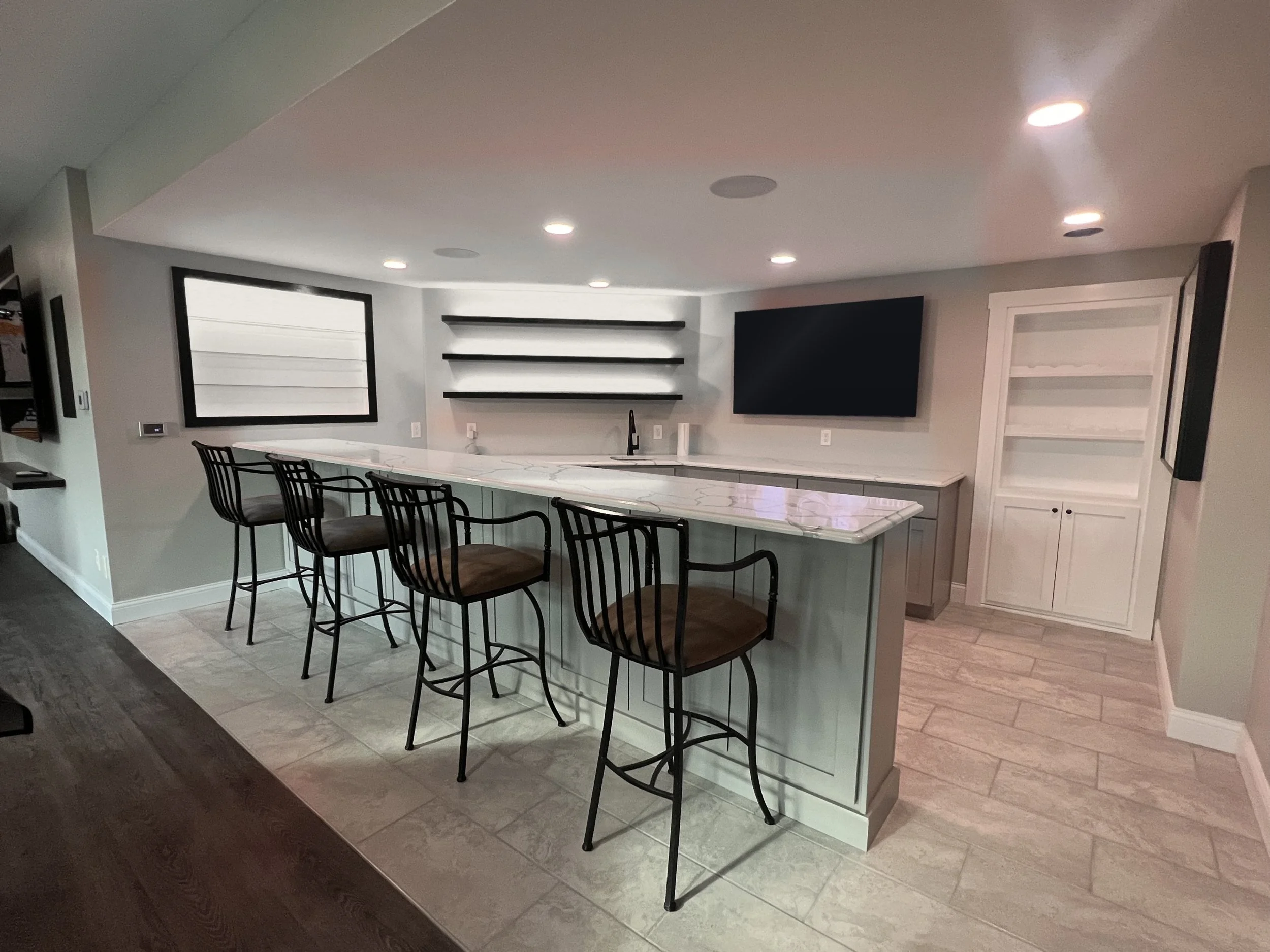 Basement bar with a quartz bar top, seating for four, and white-lit floating shelves and display case
