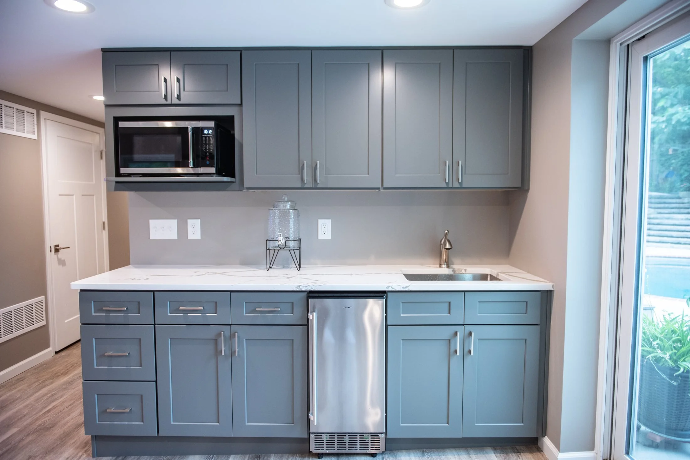 Basement kitchenette with gray cabinetry and a microwave