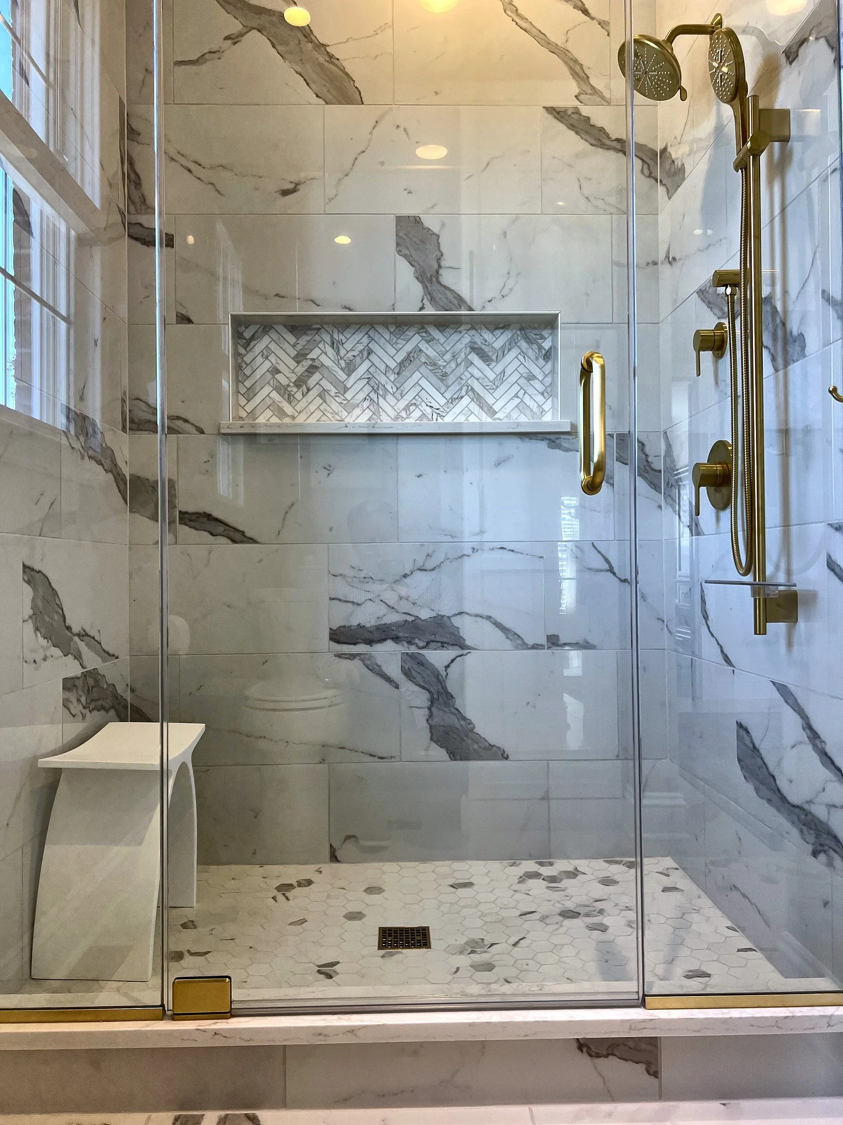 Frameless glass shower with brass fixtures and a herringbone niche