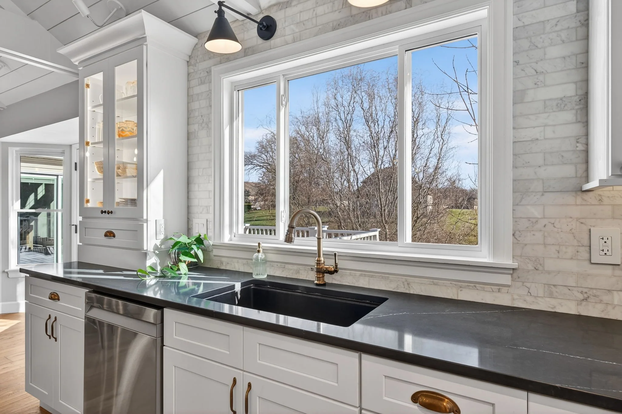 Kitchen sink under a large window with dark countertops