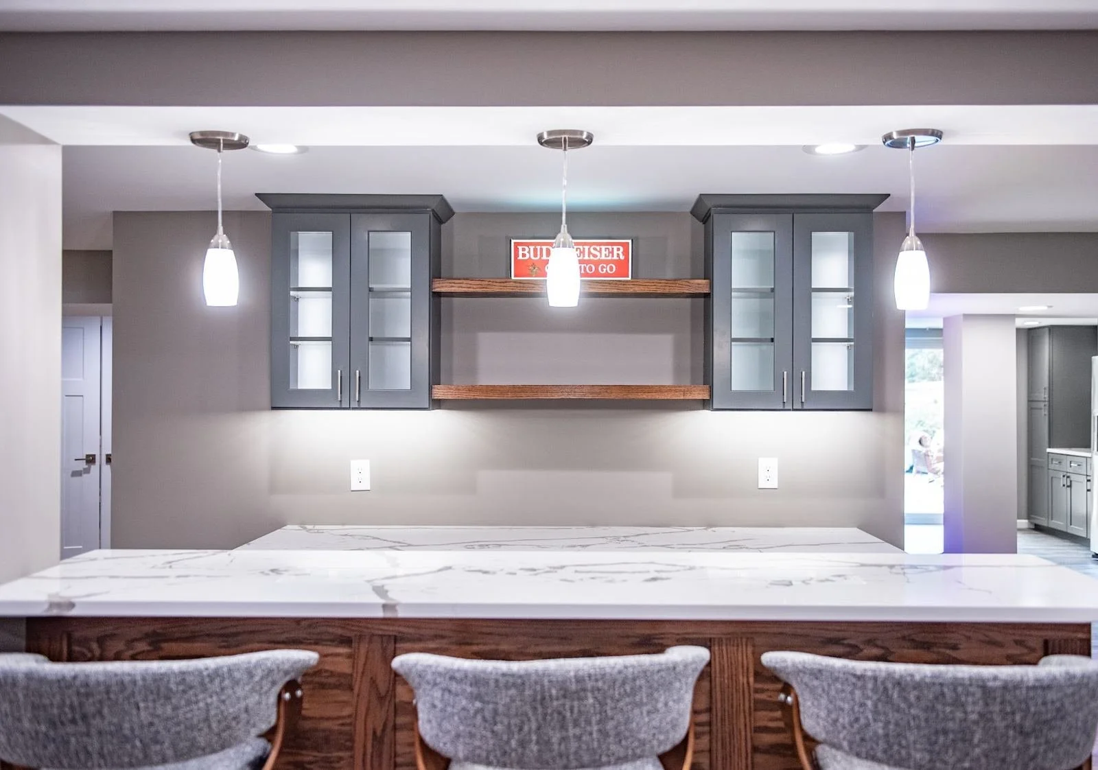 Finished basement wet bar with glass-front cabinets and pendant lights