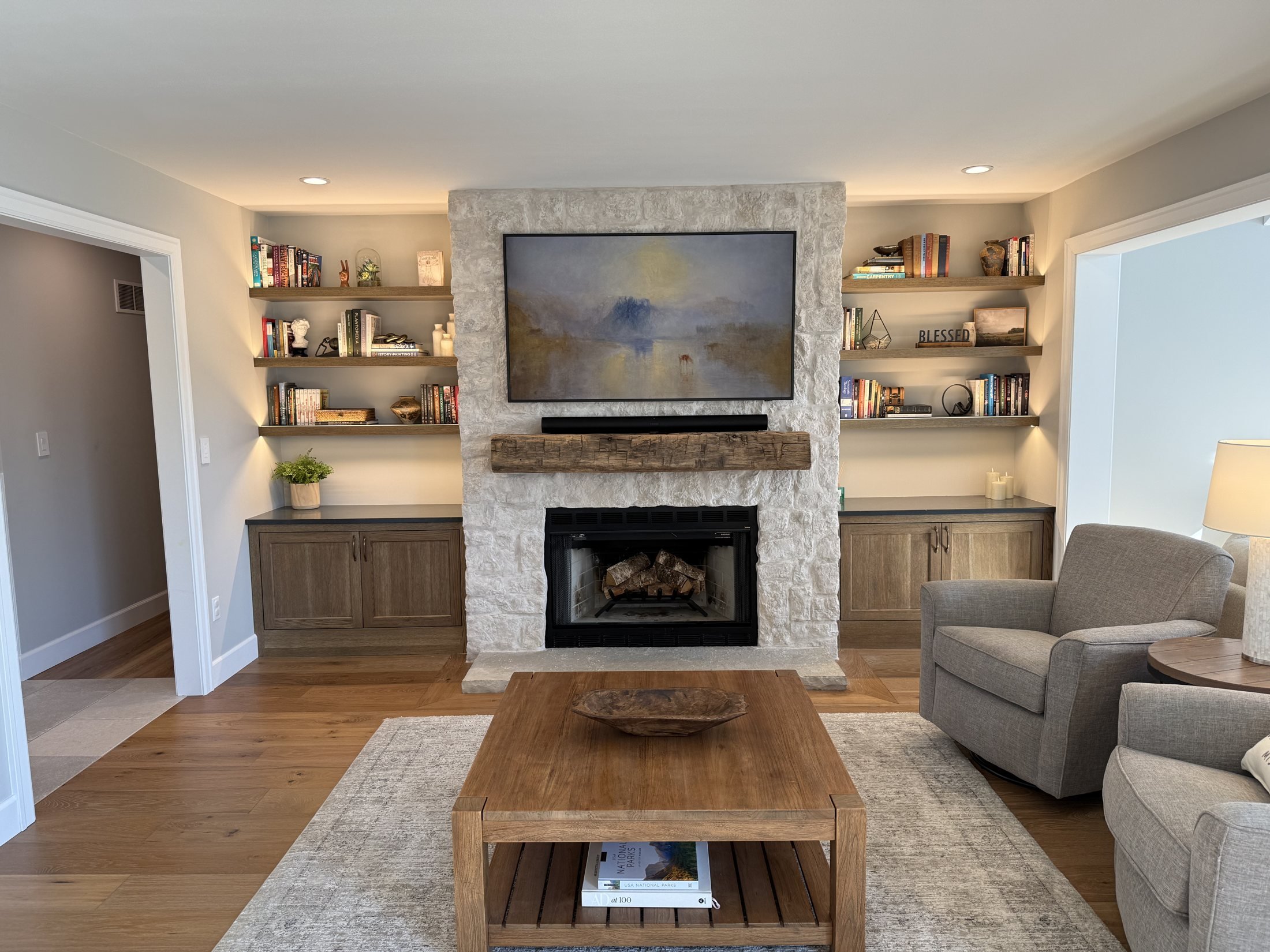 Family room with a stone fireplace and lit floating shelves