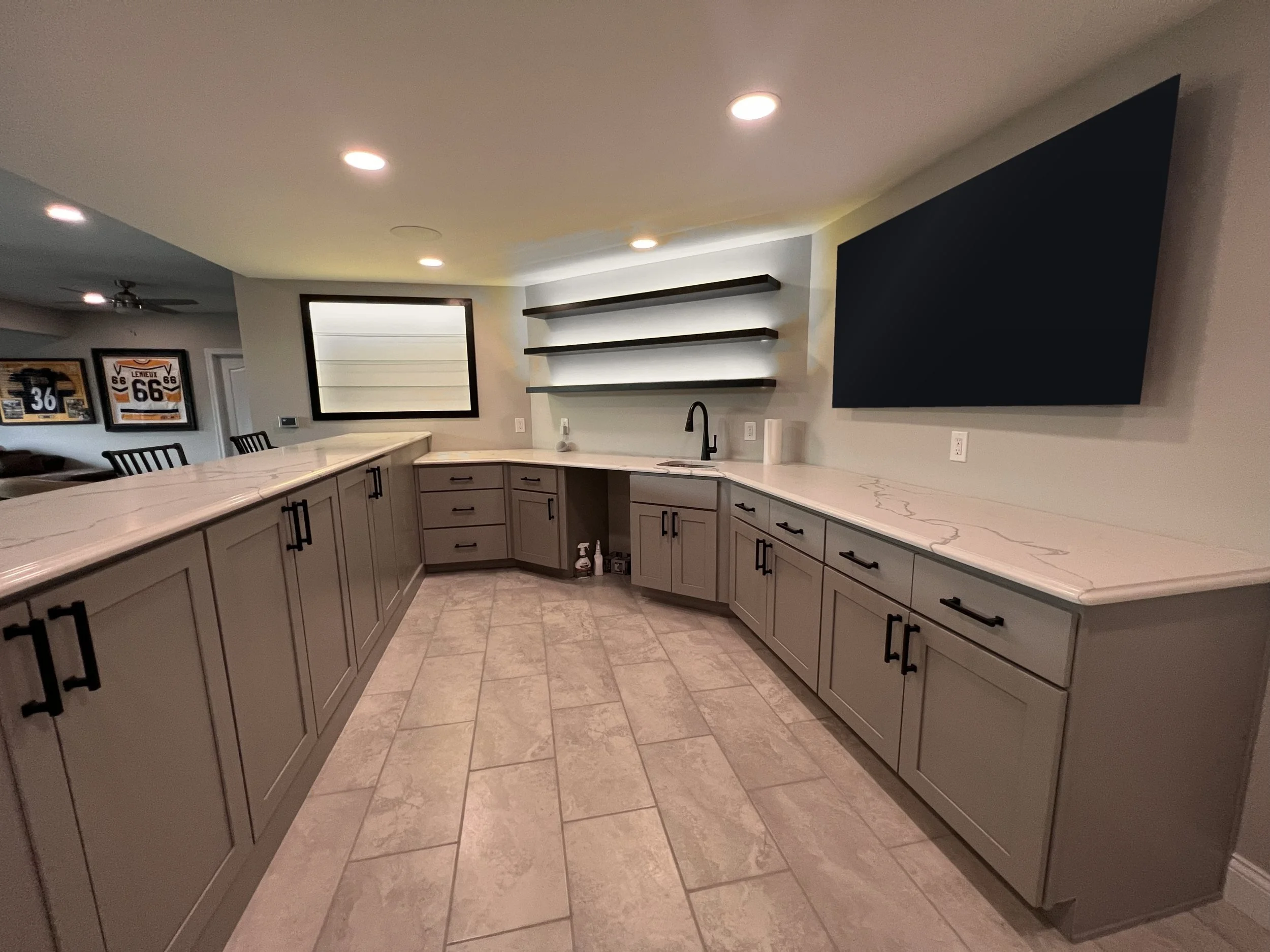 Wet bar with gray shaker cabinets, black hardware, and white-lit floating shelves