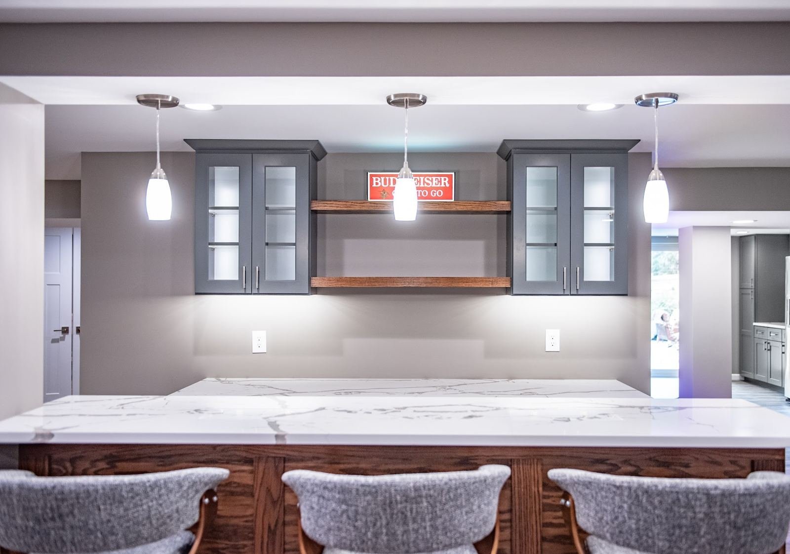 Finished basement wet bar with glass-front cabinets and pendant lights