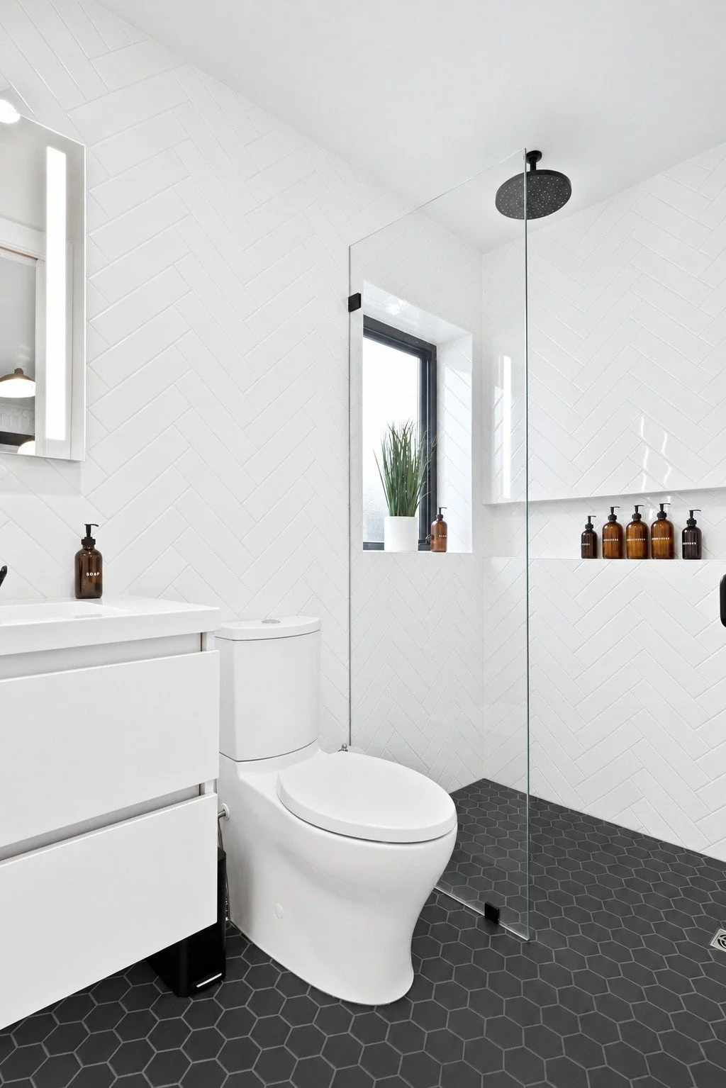 White herringbone tile walk-in shower with a black hex tile floor and a rain shower head