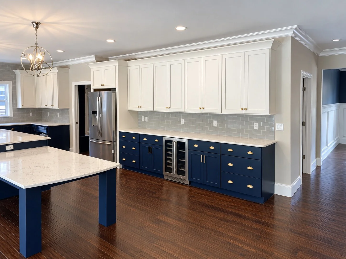 White shaker uppers, navy lowers with brass pulls, and a beverage fridge