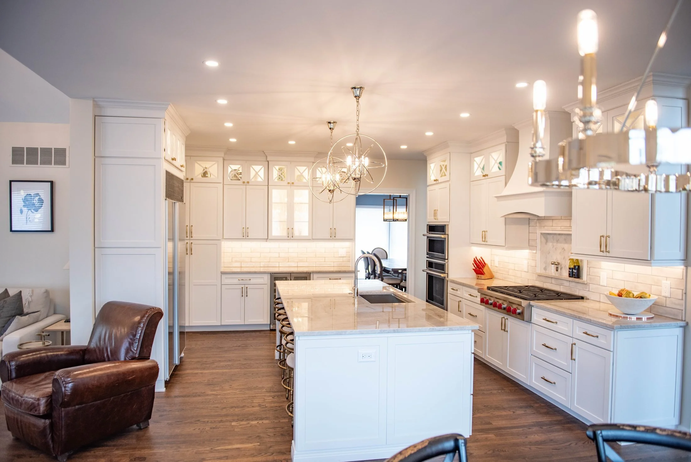 White kitchen with a quartz island, globe pendants, and glass-front cabinets