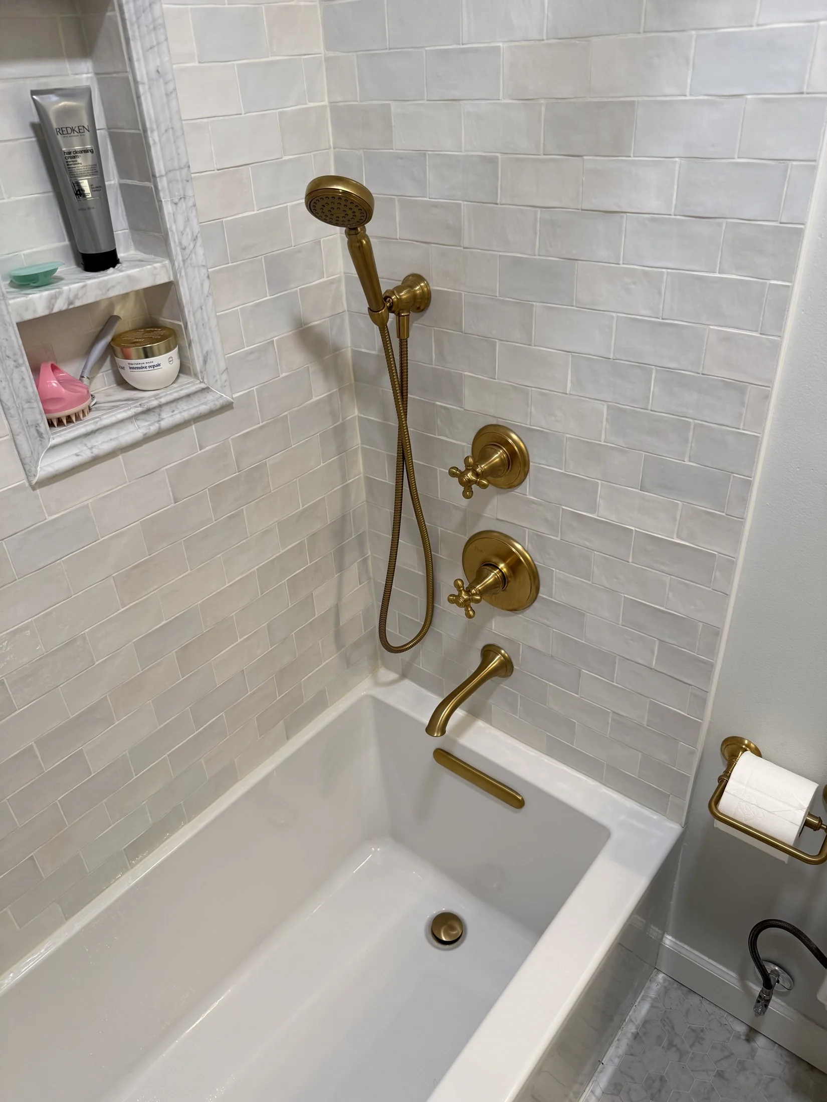 Glossy white tile tub surround with brass fixtures