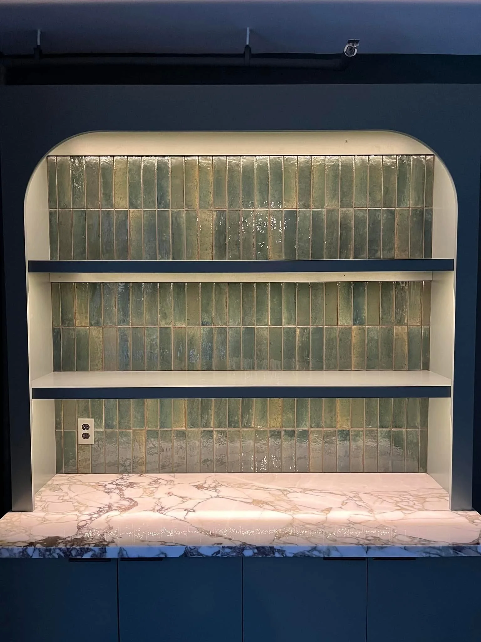 Arched bookcase with lit shelves and a stone countertop