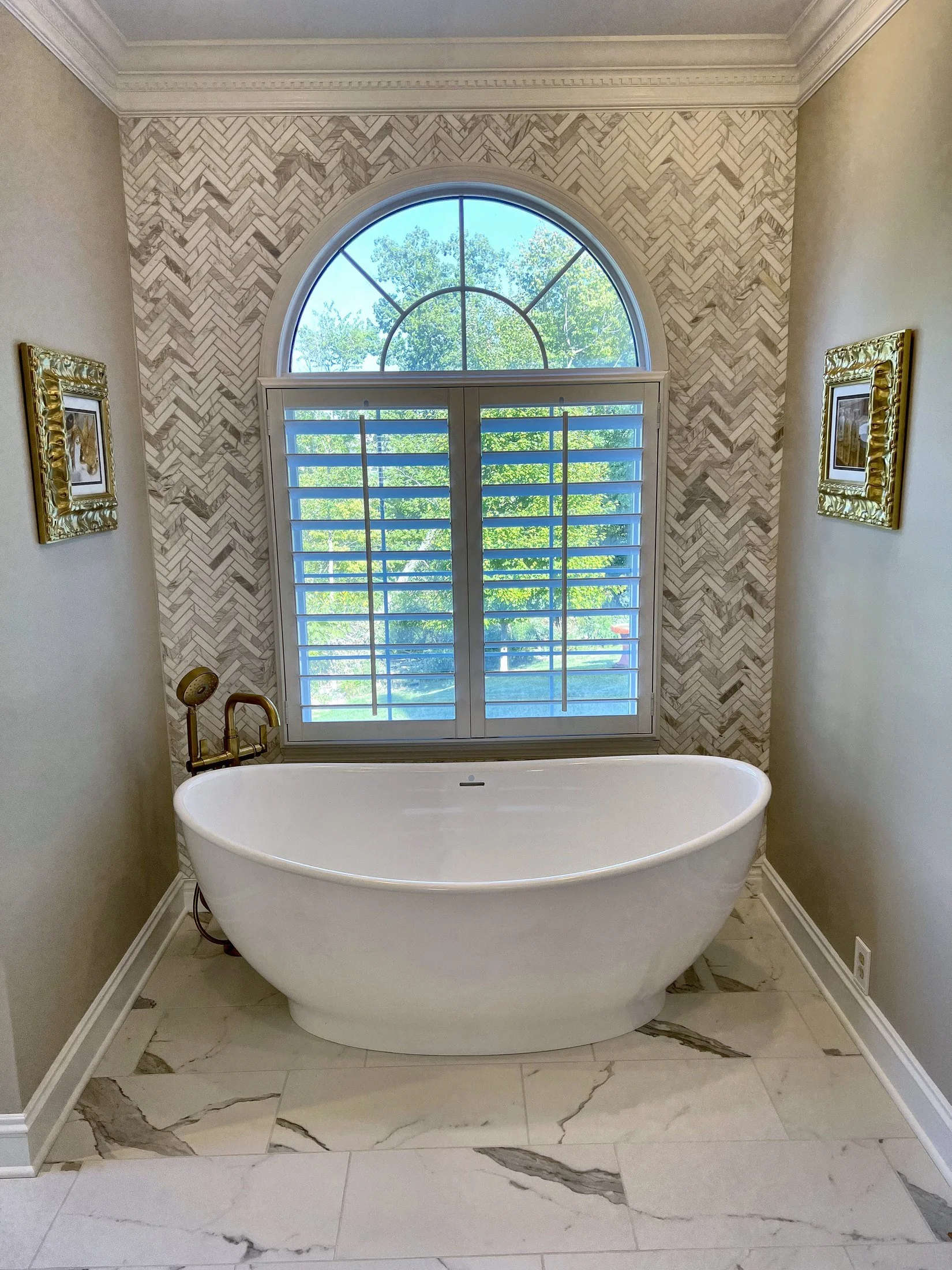 Freestanding tub under an arched window with a herringbone tile wall