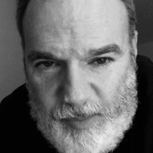 Retrato en blanco y negro de un hombre de cabello y barba canosos mirándose directamente a la cámara.