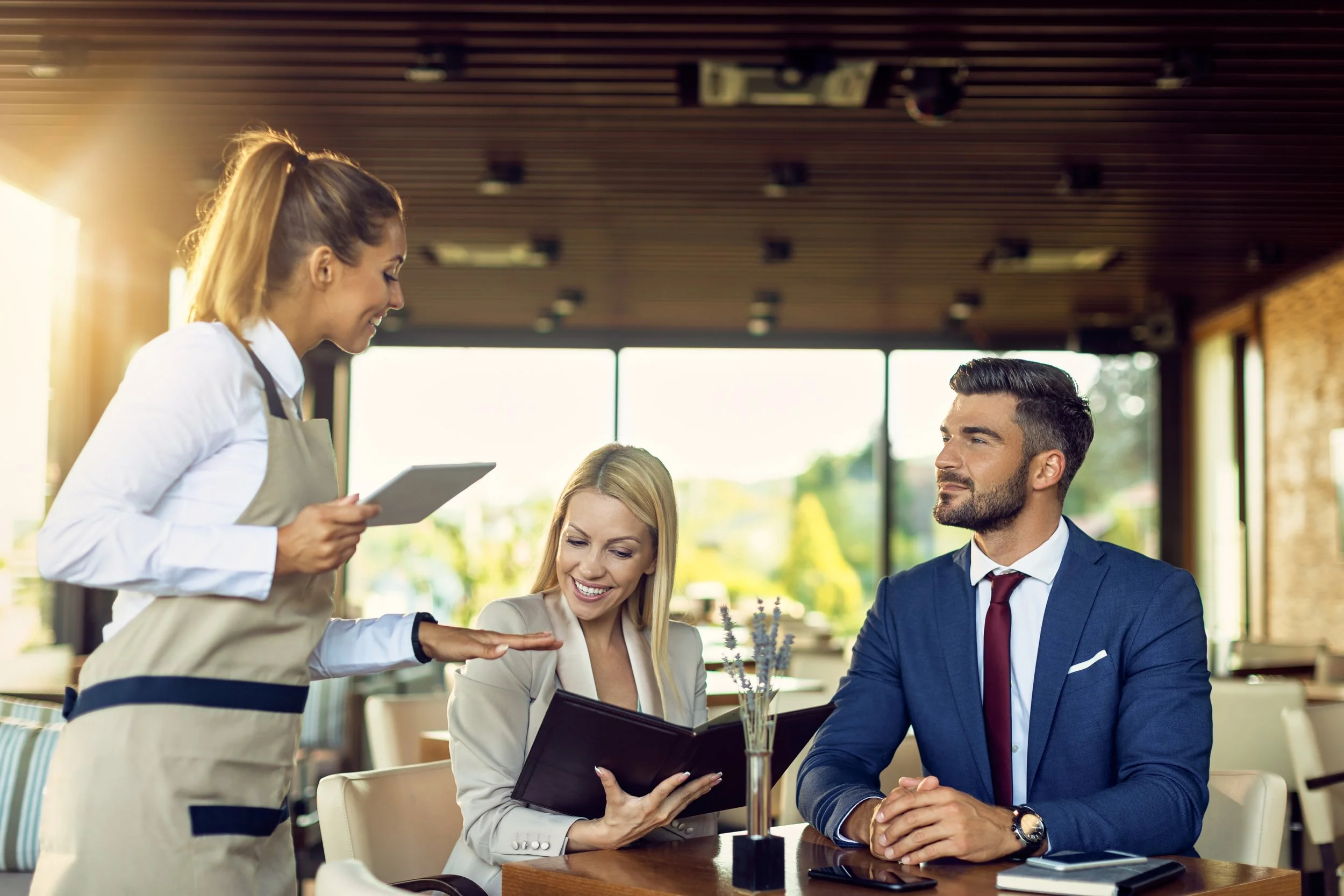 Dos personas, una mujer y un hombre, en una comida en un restaurante, la mujer muestra una carta y el hombre la mira, mientras una camarera los atiende.