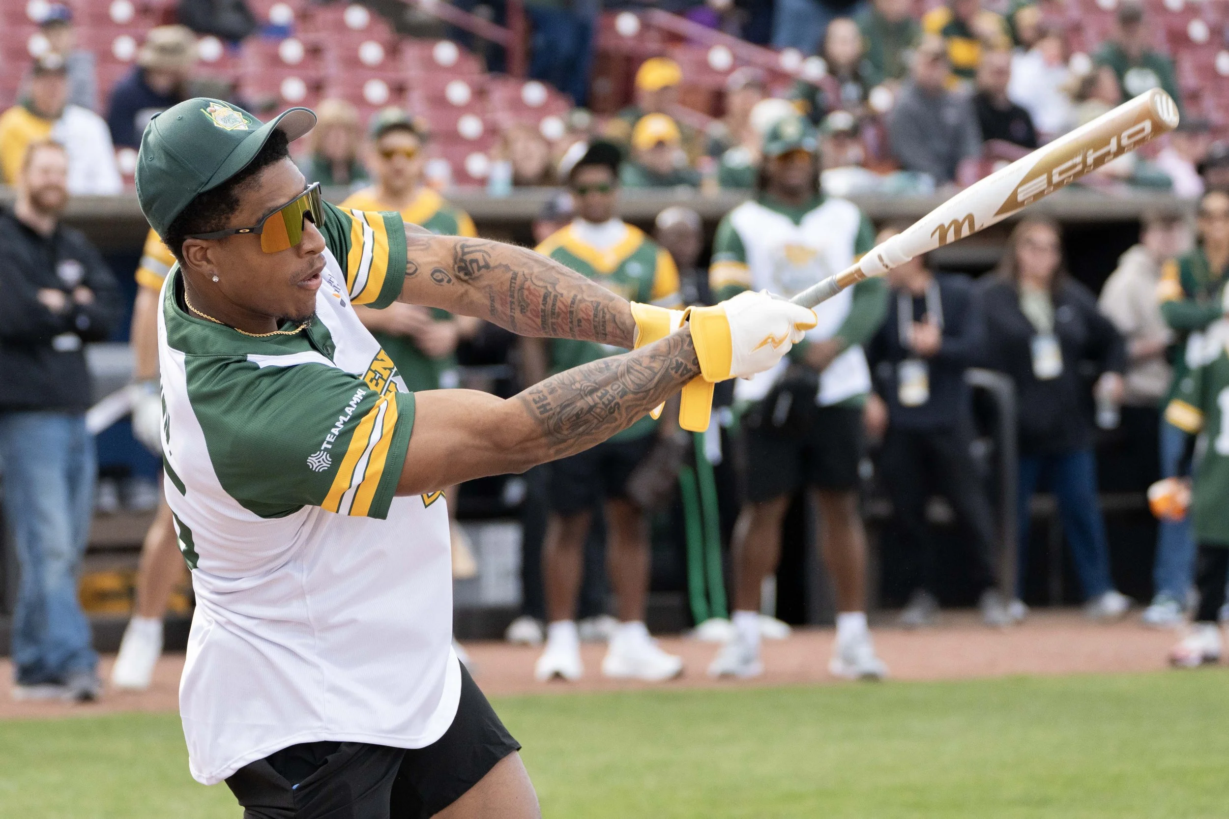 A man in sports attire swinging a baseball bat at a baseball game, with spectators in the background.