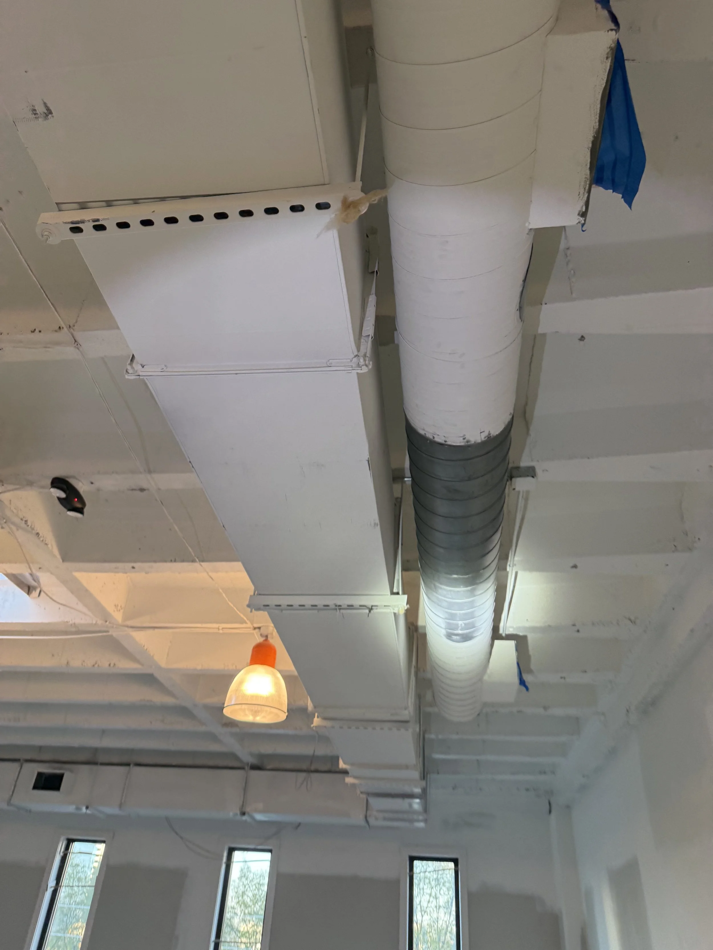 Suspended ceiling with HVAC ductwork, ceiling tiles, and a hanging light fixture in a building under construction or renovation.