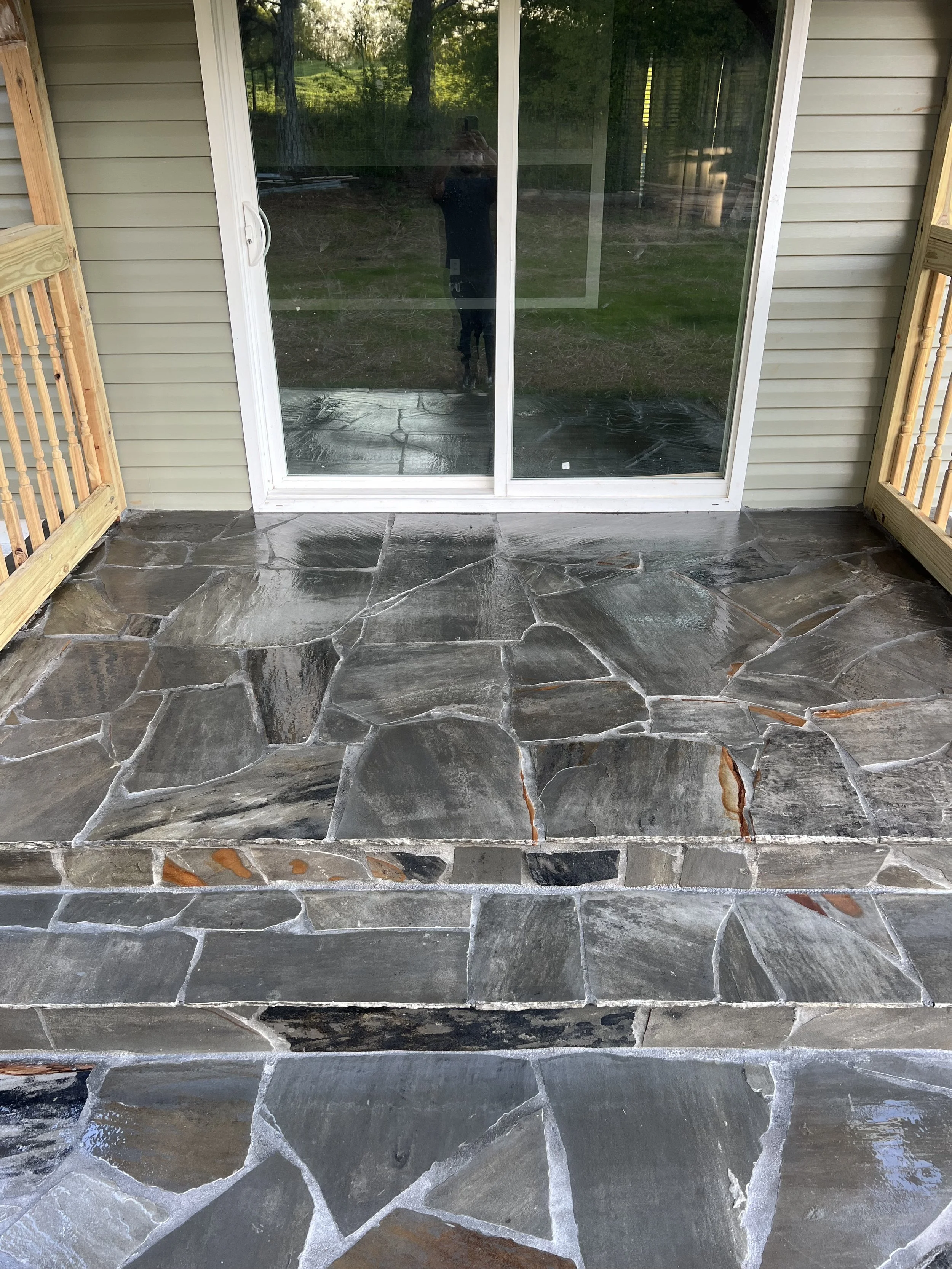 Newly installed flagstone patio in front of a sliding glass door, with wooden railing on either side, attached to a house with beige siding.