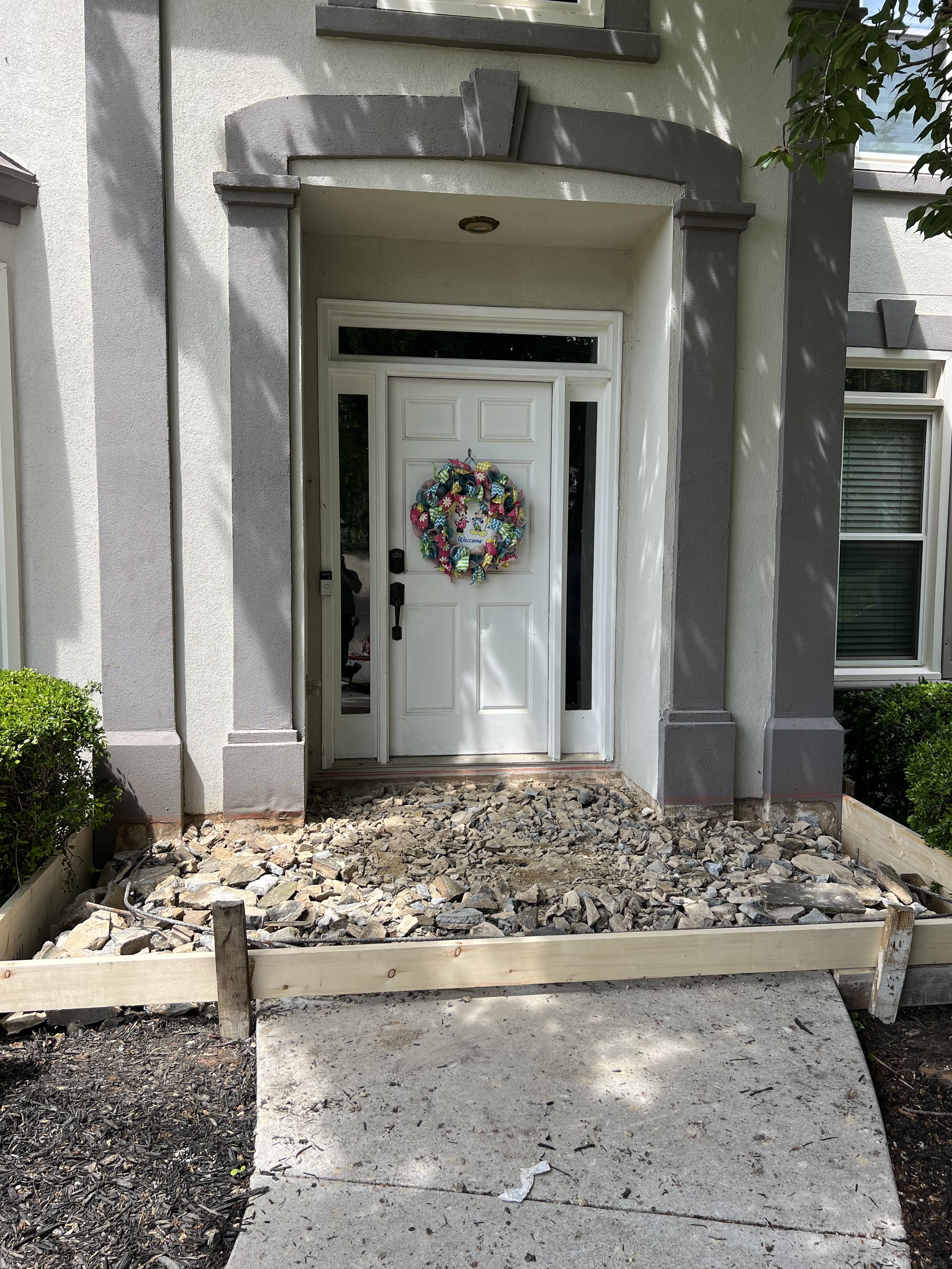 Front door of a house under renovation with a small step, stone debris in front, and a decorative wreath on the white door.