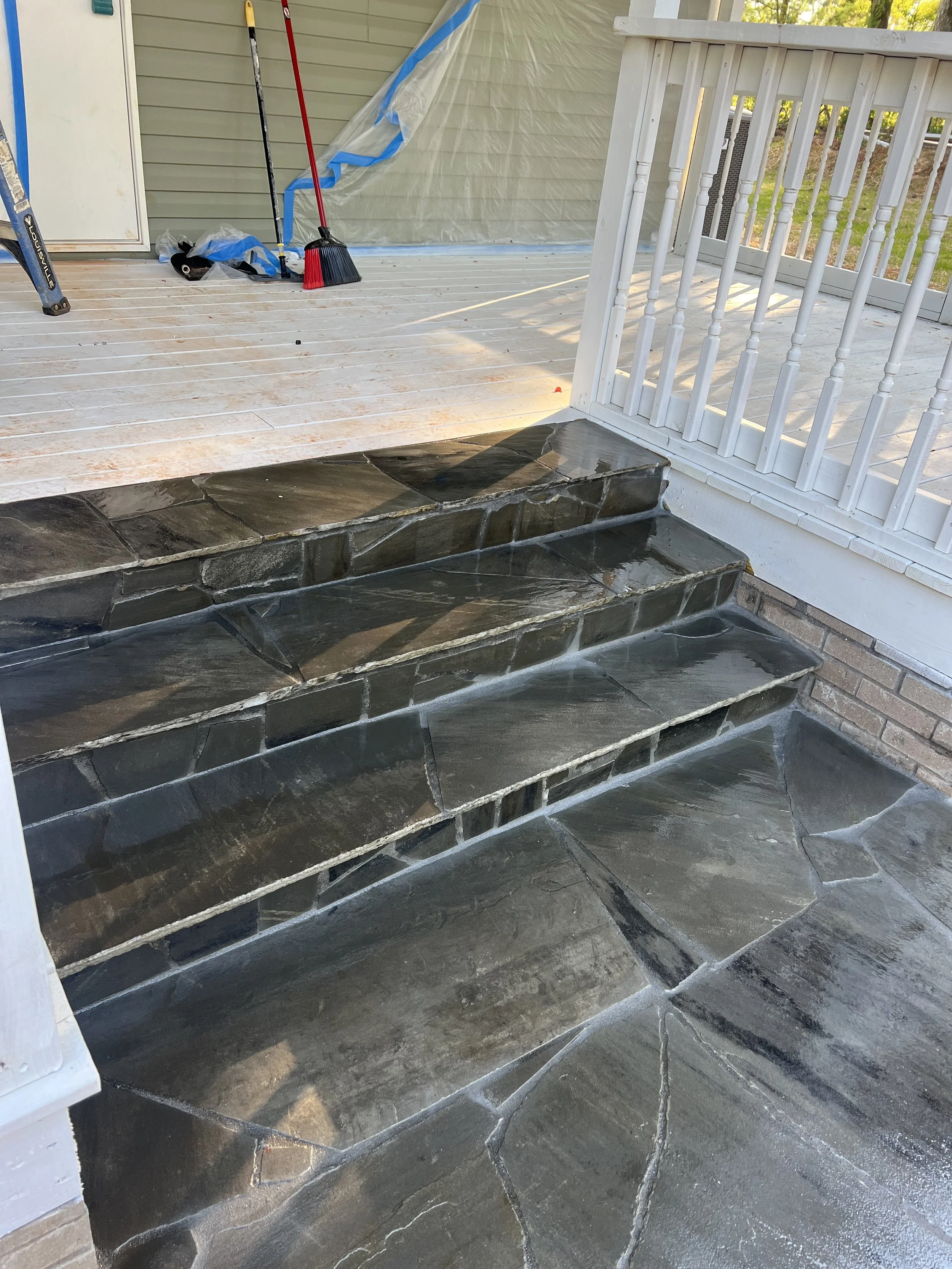 Stone outdoor stairs leading to a porch, with cleaning supplies and a broom visible in the background.